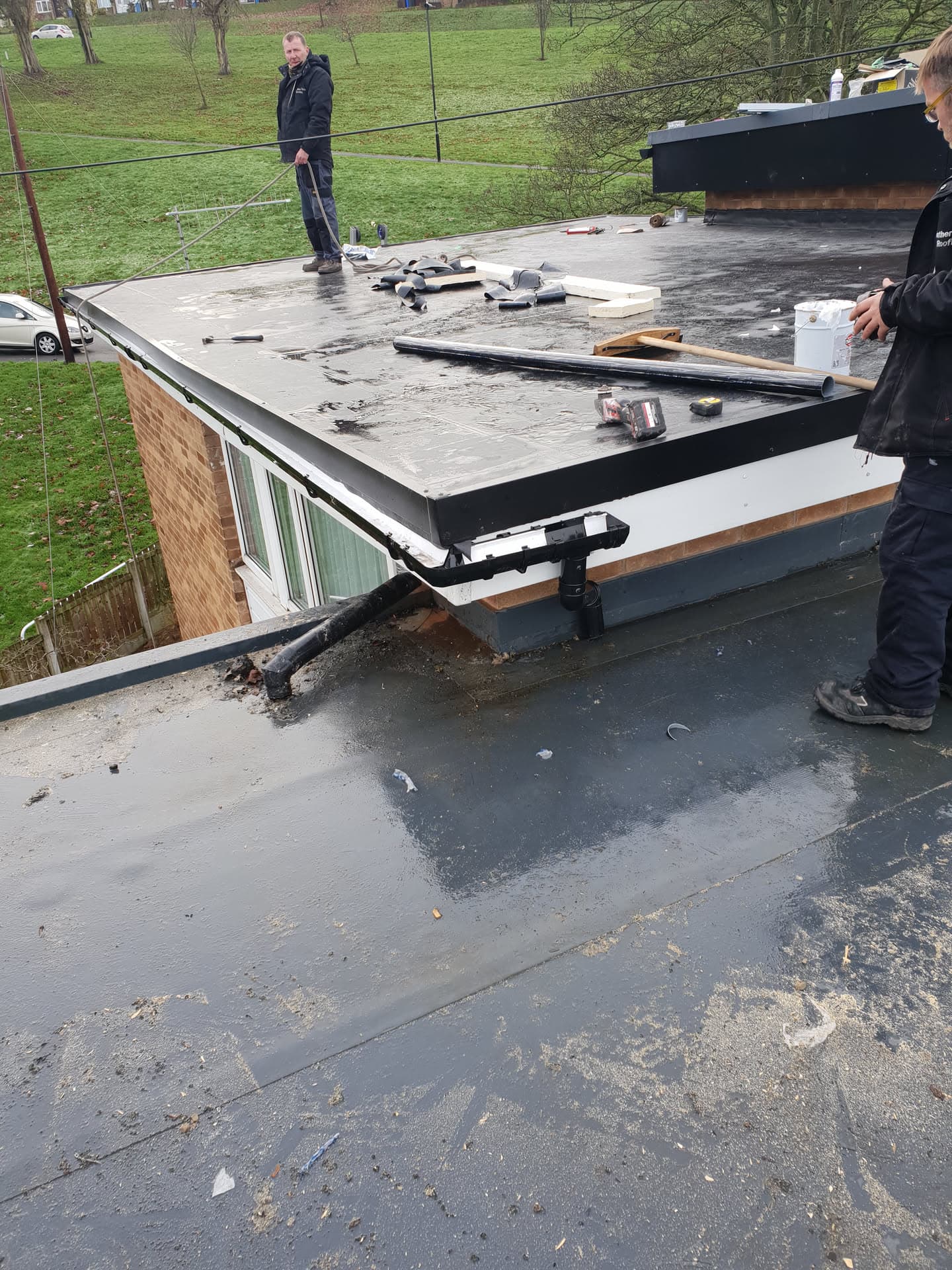 Fitters installing GRP fibreglass flat roof on extension with black fascia trim