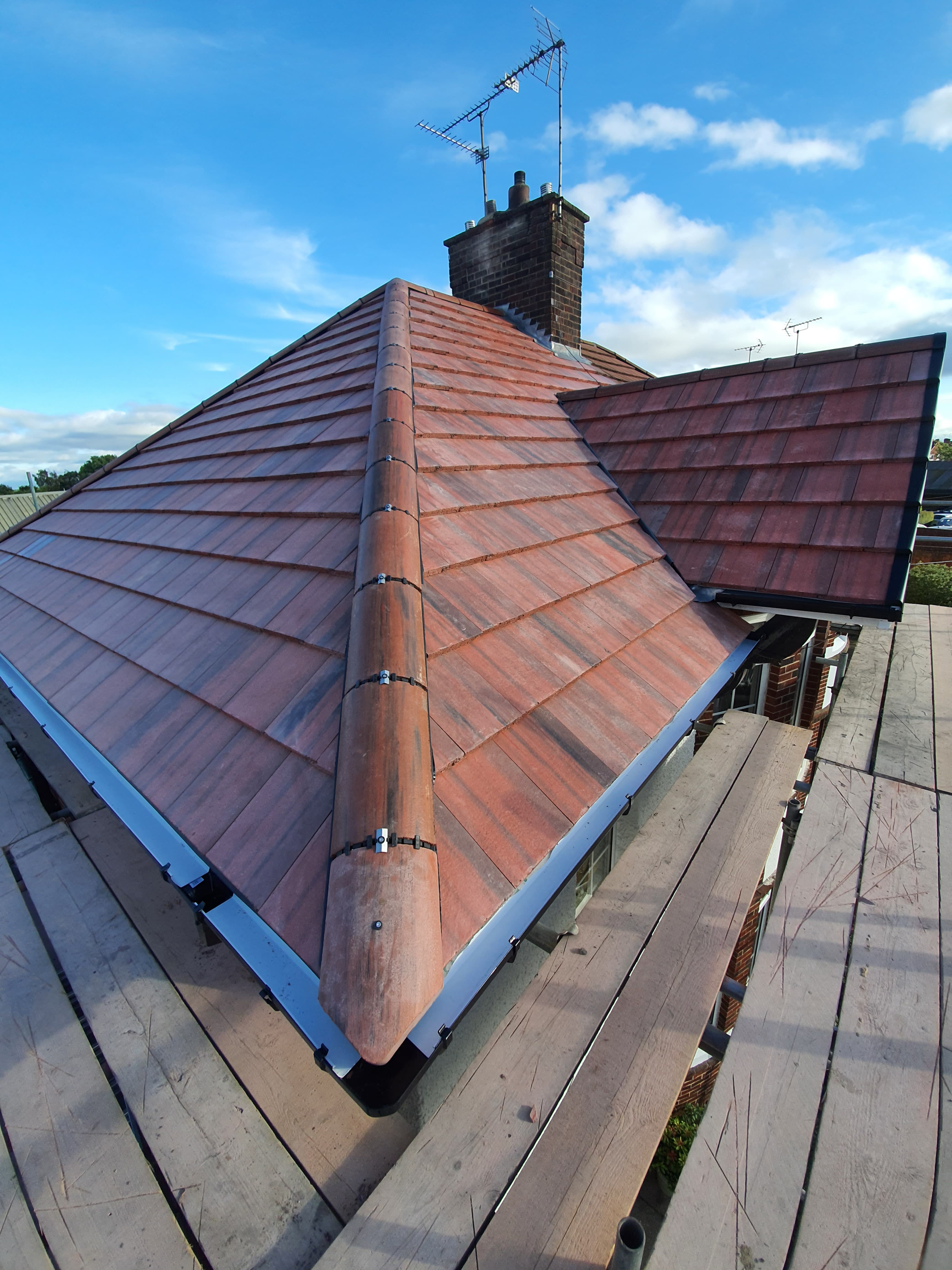 Pitched roof with terracotta clay tiles, ridge tiles and chimney stack with TV aerial
