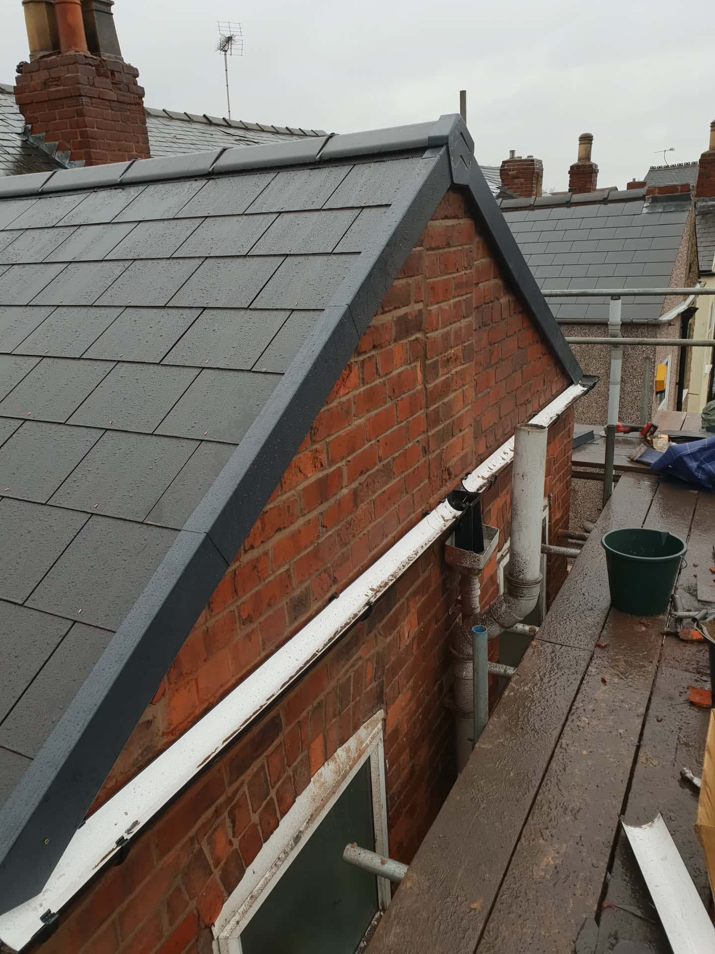 Newly installed grey slate pitched roof with lead flashing and brick chimney stack