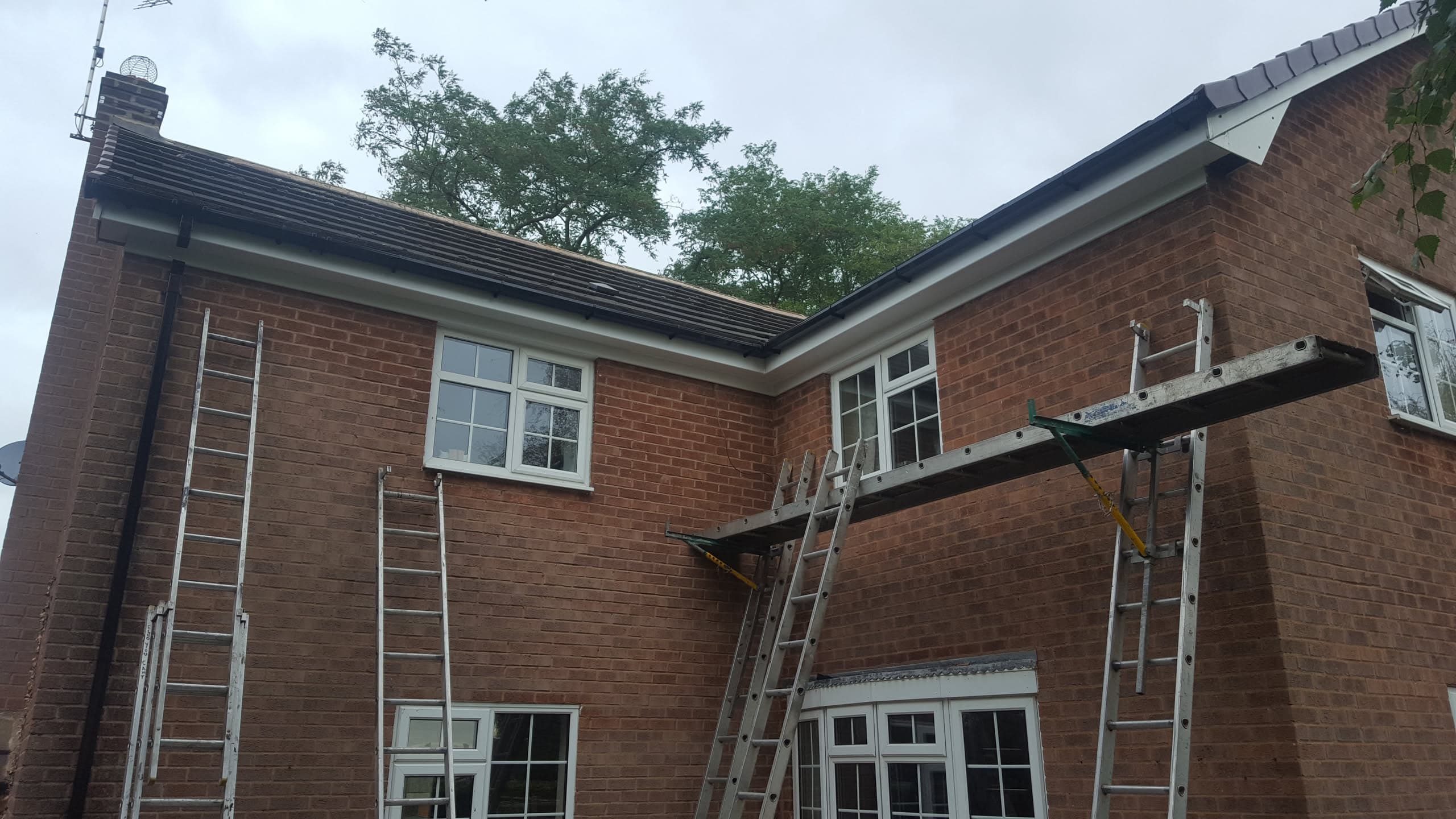 Dark grey tiled pitched roof on red brick house with black guttering and downpipes