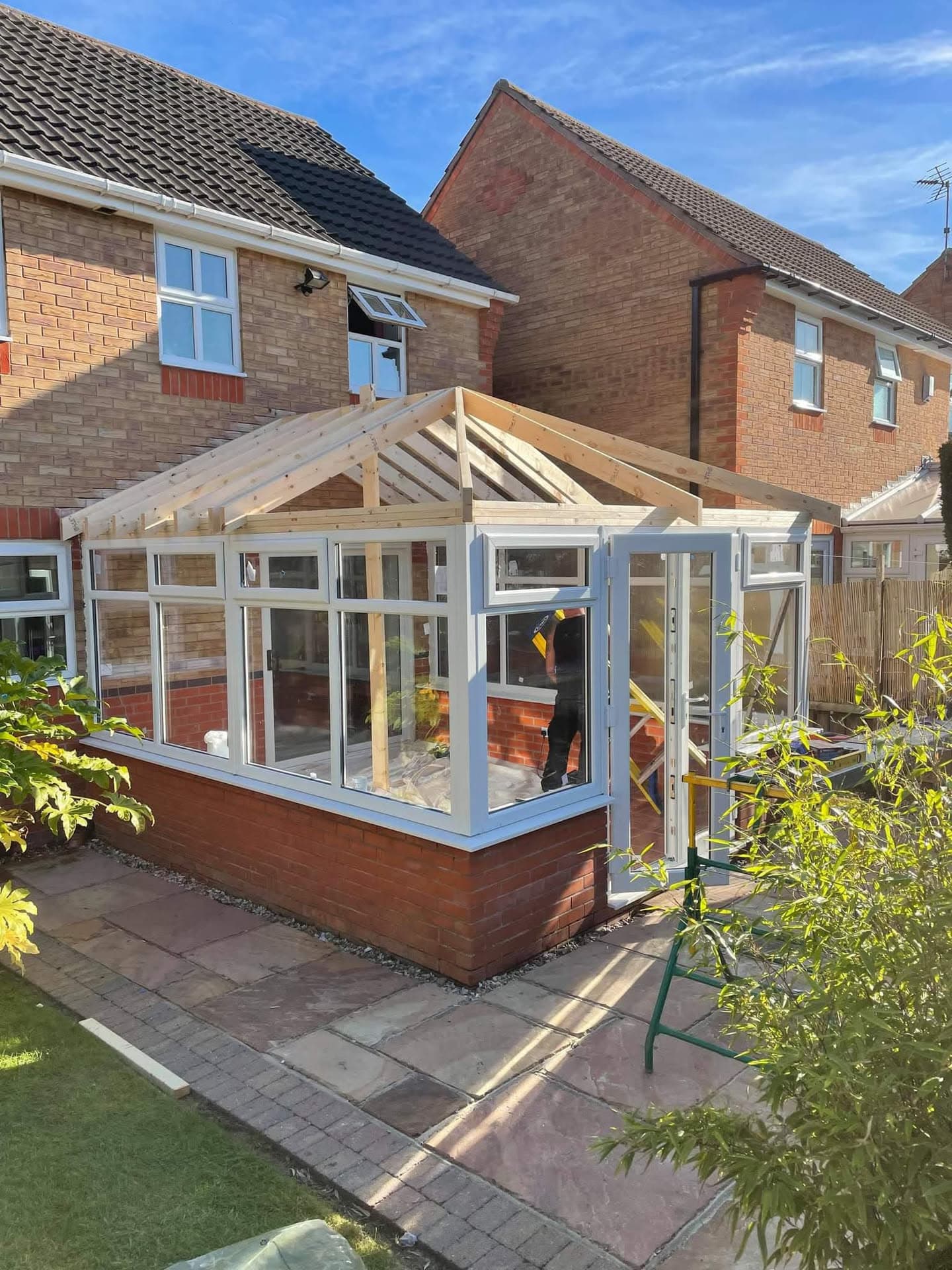 Conservatory with timber frame roof structure under construction on brick house with tiled roof