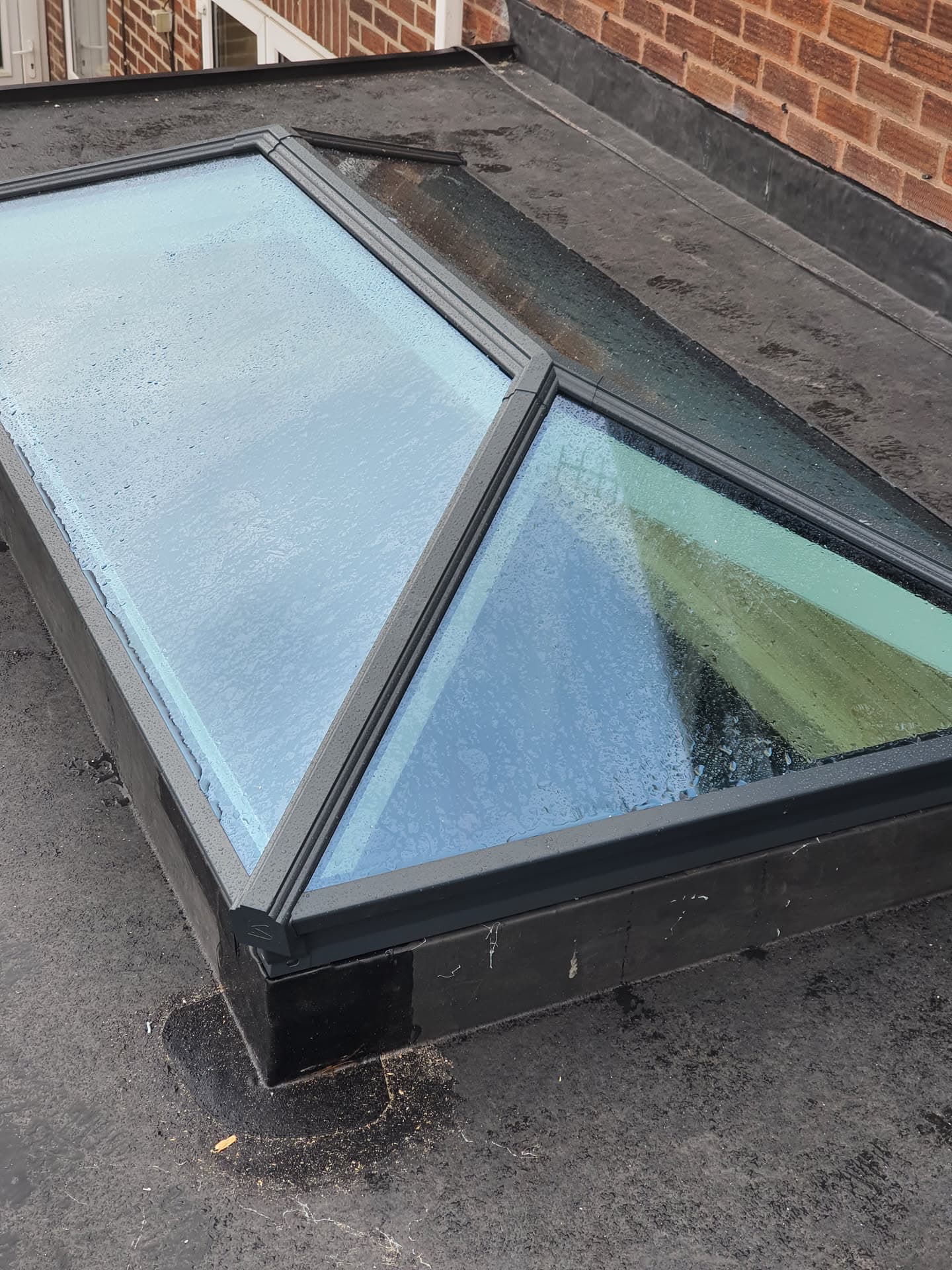 Flat roof with glass rooflight and lead flashing against brick wall