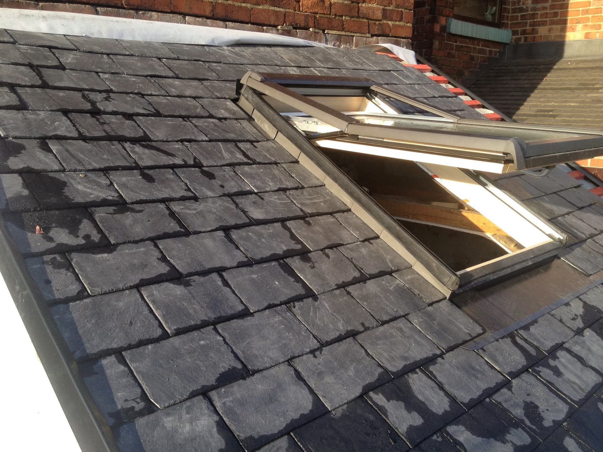 Pitched slate roof with open roof window frame during installation