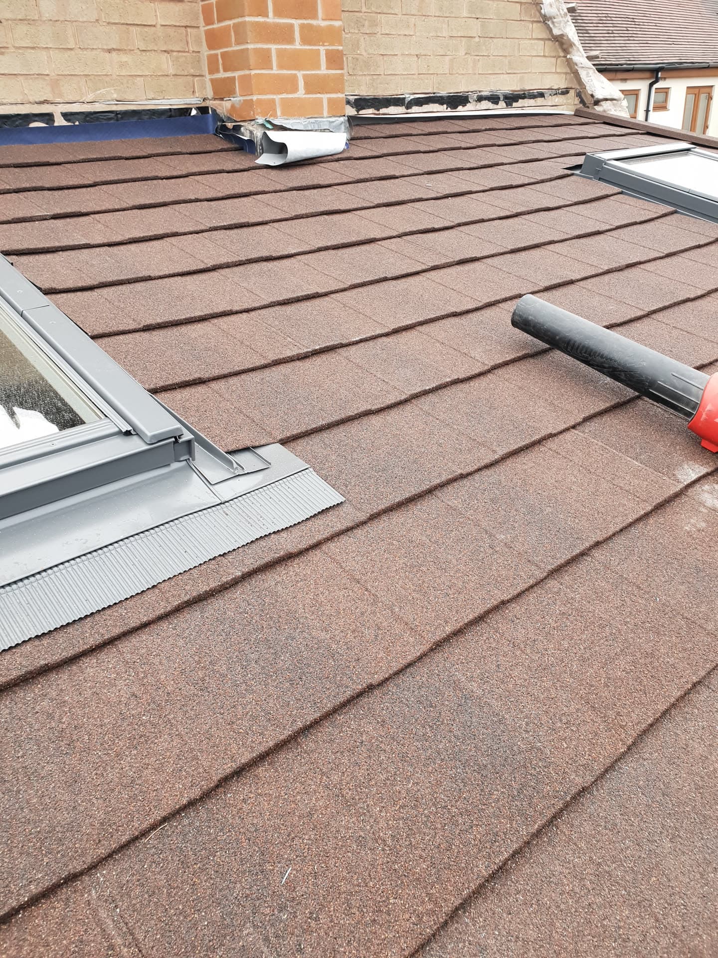 Flat roof with brown mineral felt covering and metal flashing around velux windows
