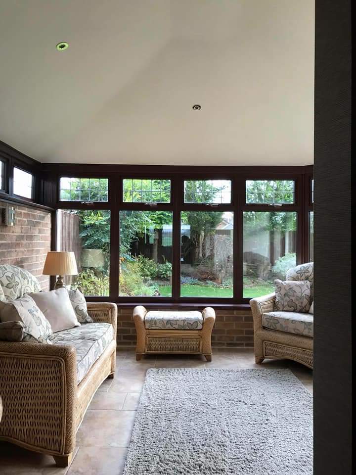 Interior view of conservatory with white plastered ceiling and dark brown window frames