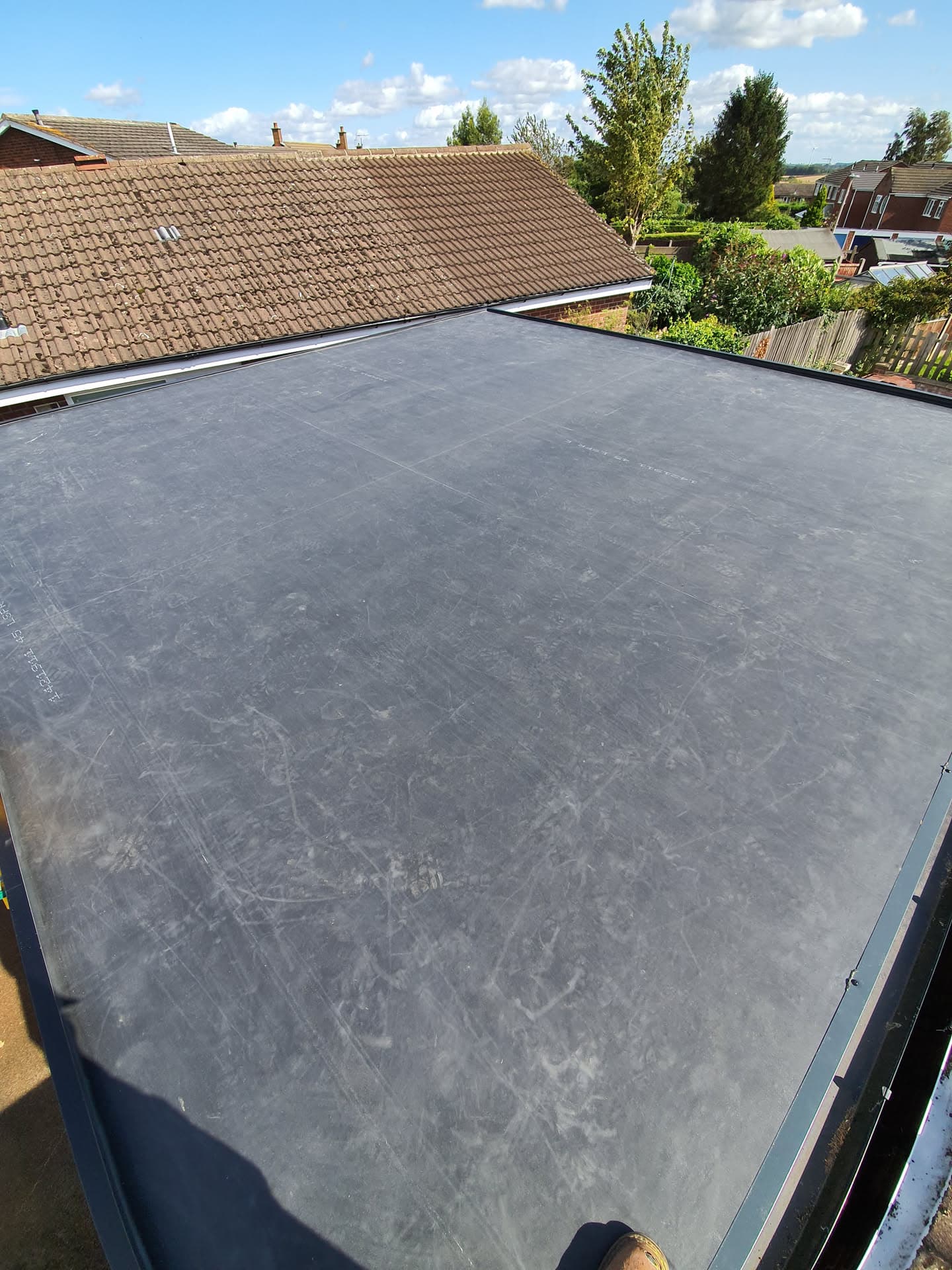 Flat roof with grey EPDM rubber membrane adjoining pitched tiled roof