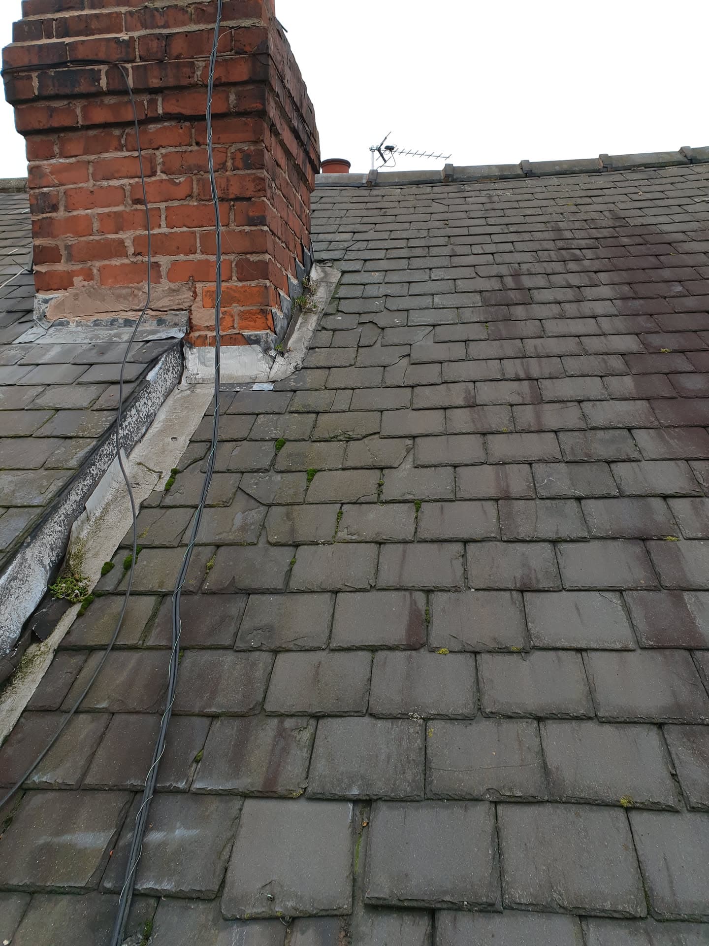Pitched roof with grey concrete tiles and red brick chimney stack with lead flashing