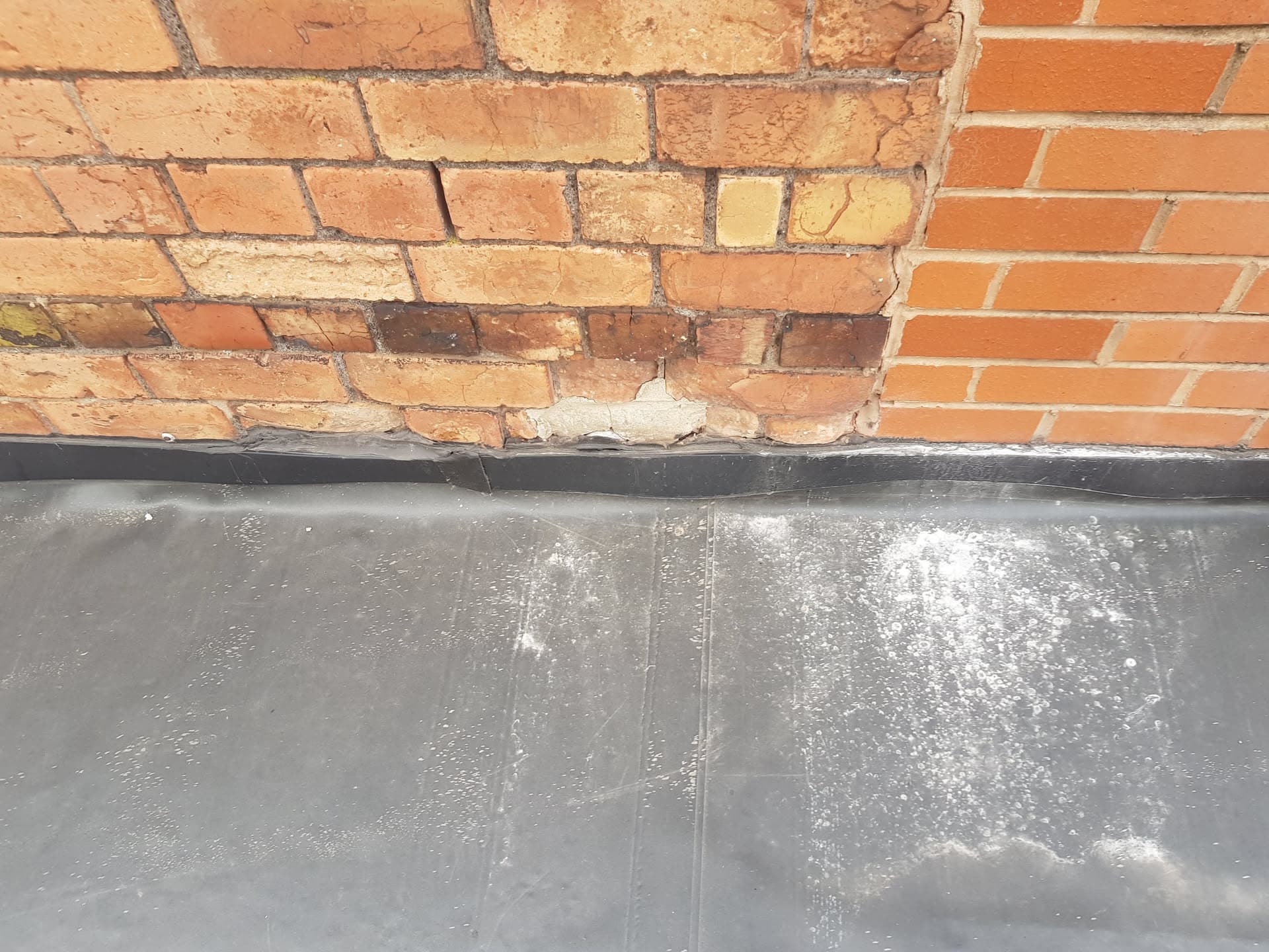 Lead flashing installed against brick chimney stack on flat roof
