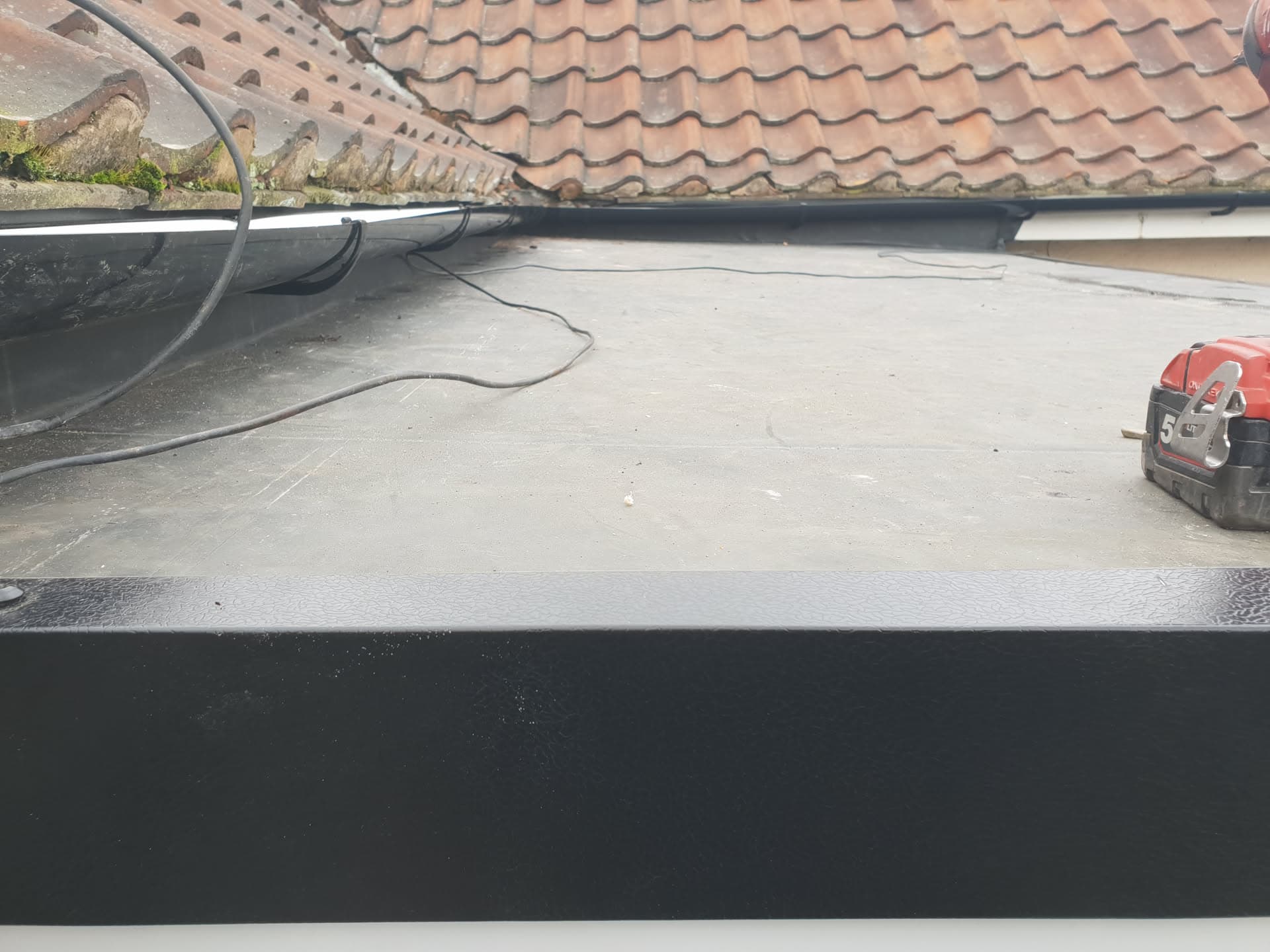 Flat roof with light grey GRP fibreglass surface and black fascia board with guttering