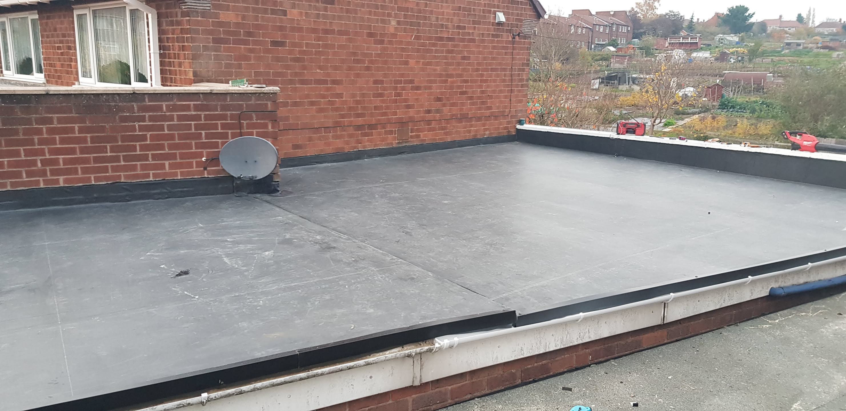 Completed flat roof installation with grey EPDM rubber membrane and black trims on residential property