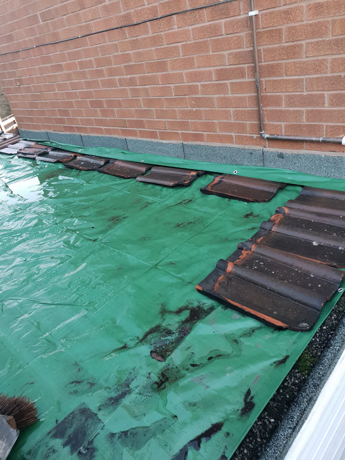 Flat roof installation in progress with green underlay and dark concrete tiles being laid