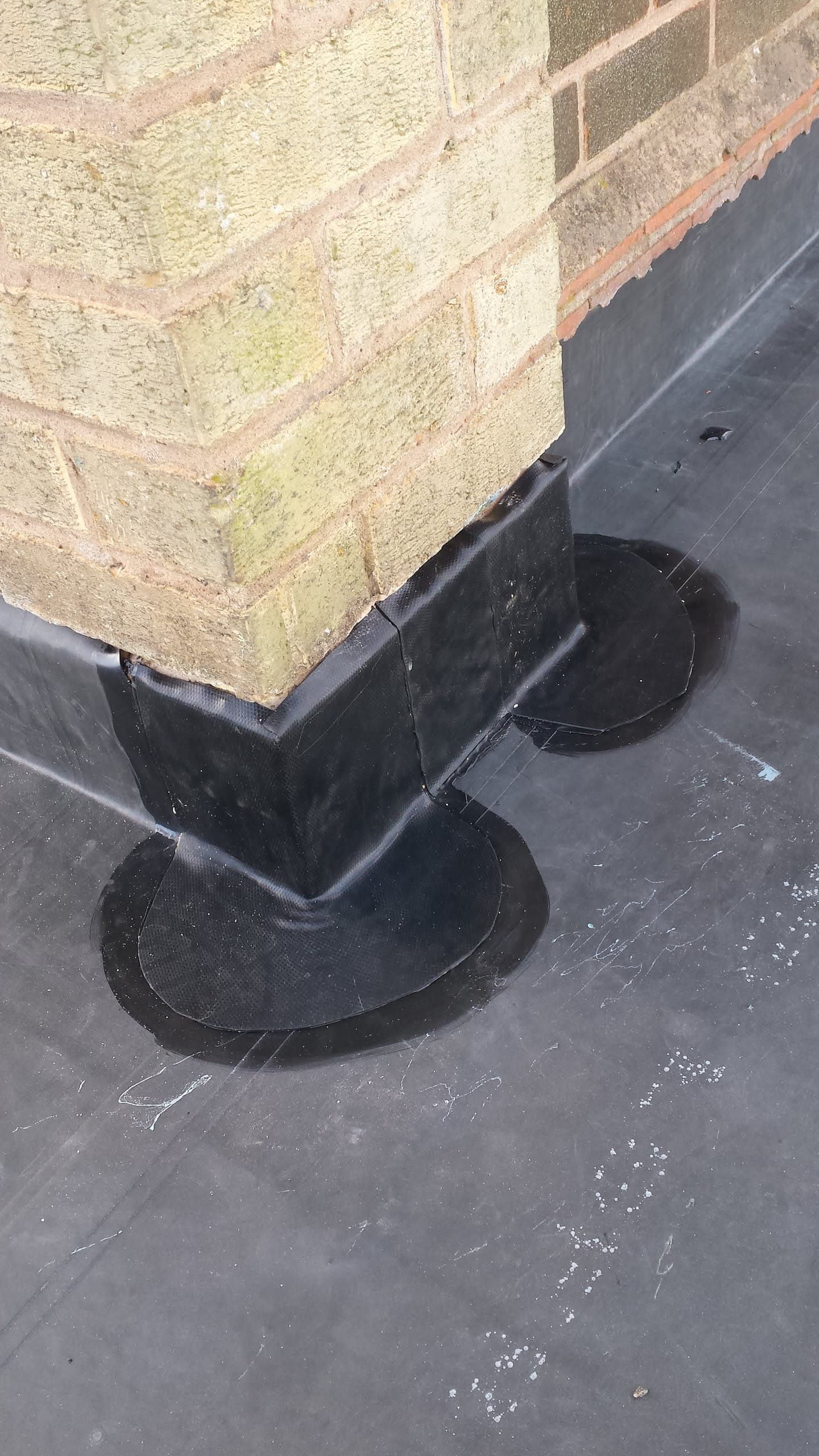 Black rubber flat roof with pipe flashing sealed against brick chimney stack