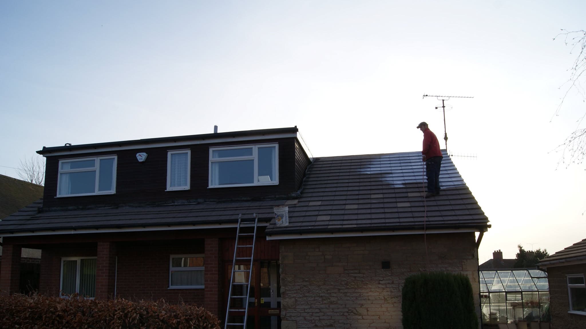 Fitter working on pitched tiled roof with ladder against property