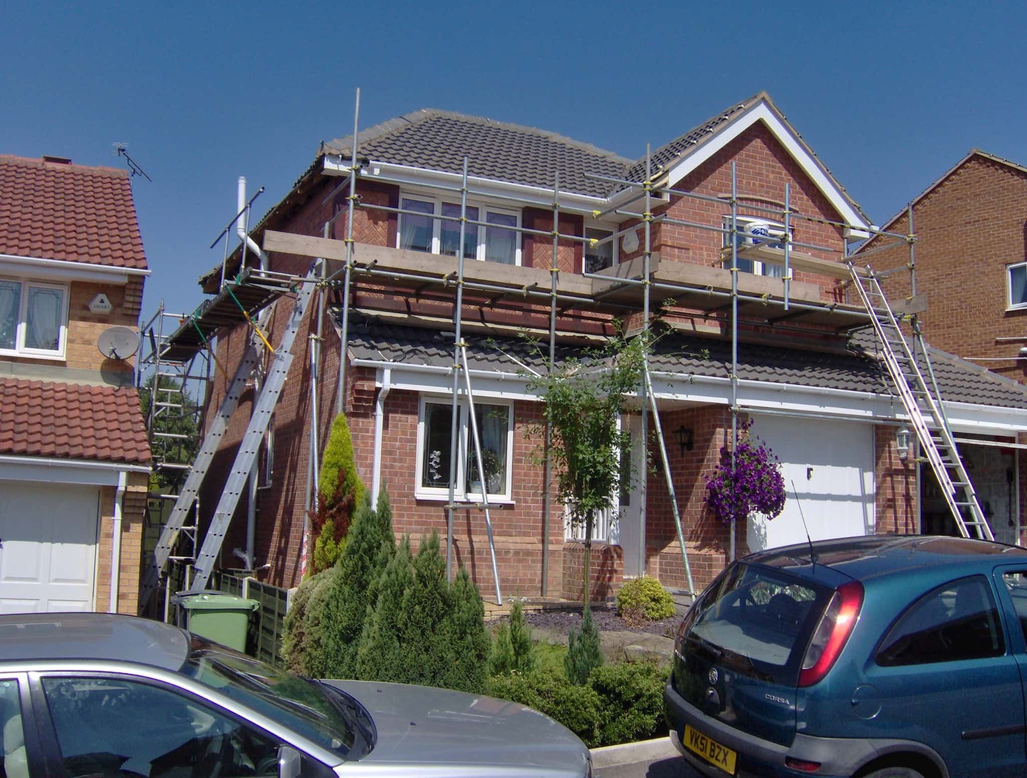 Pitched roof with grey concrete tiles and white fascias on red brick house with scaffolding
