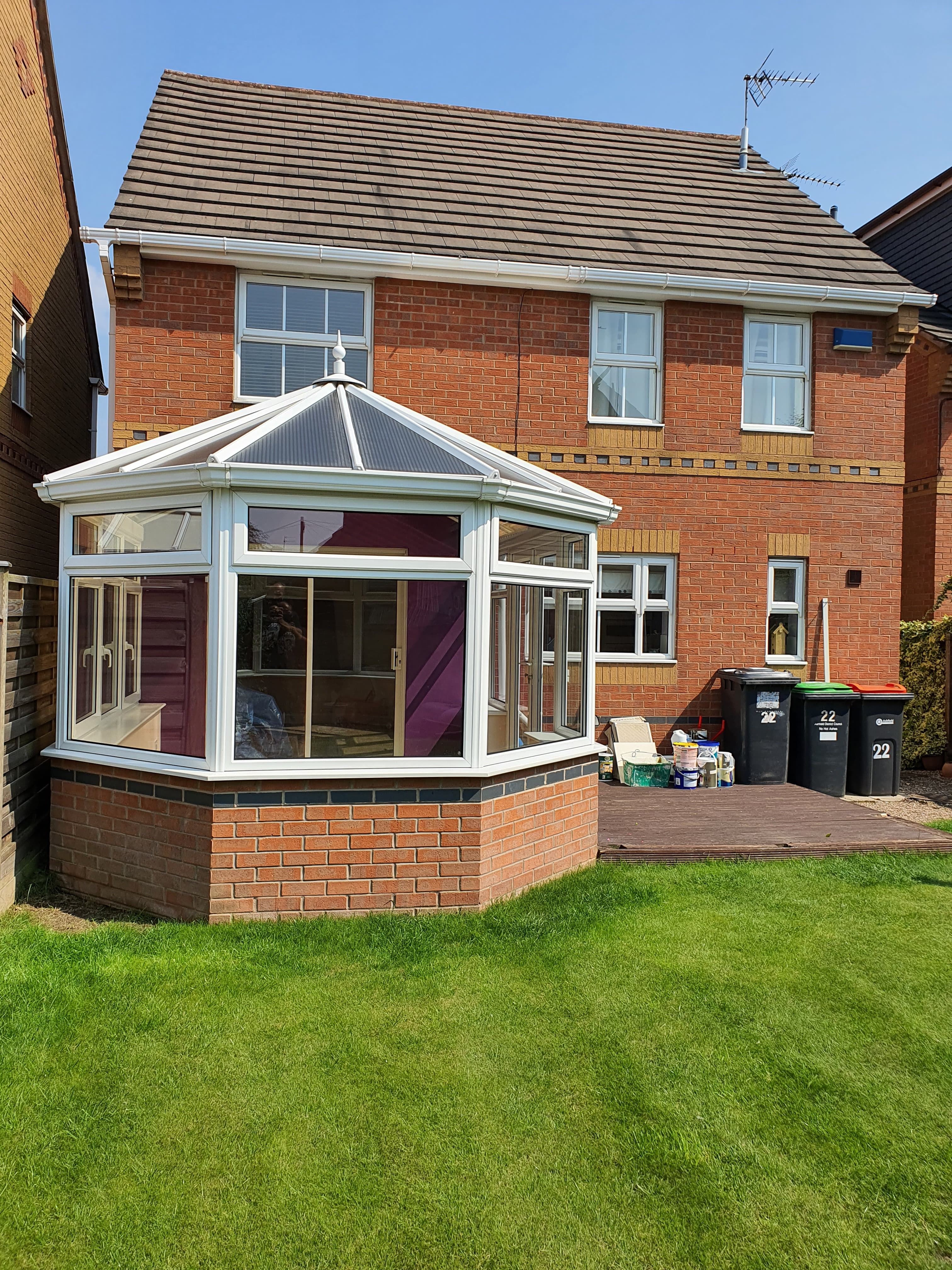 Pitched tiled roof on red brick house with white uPVC conservatory featuring grey polycarbonate roof panels