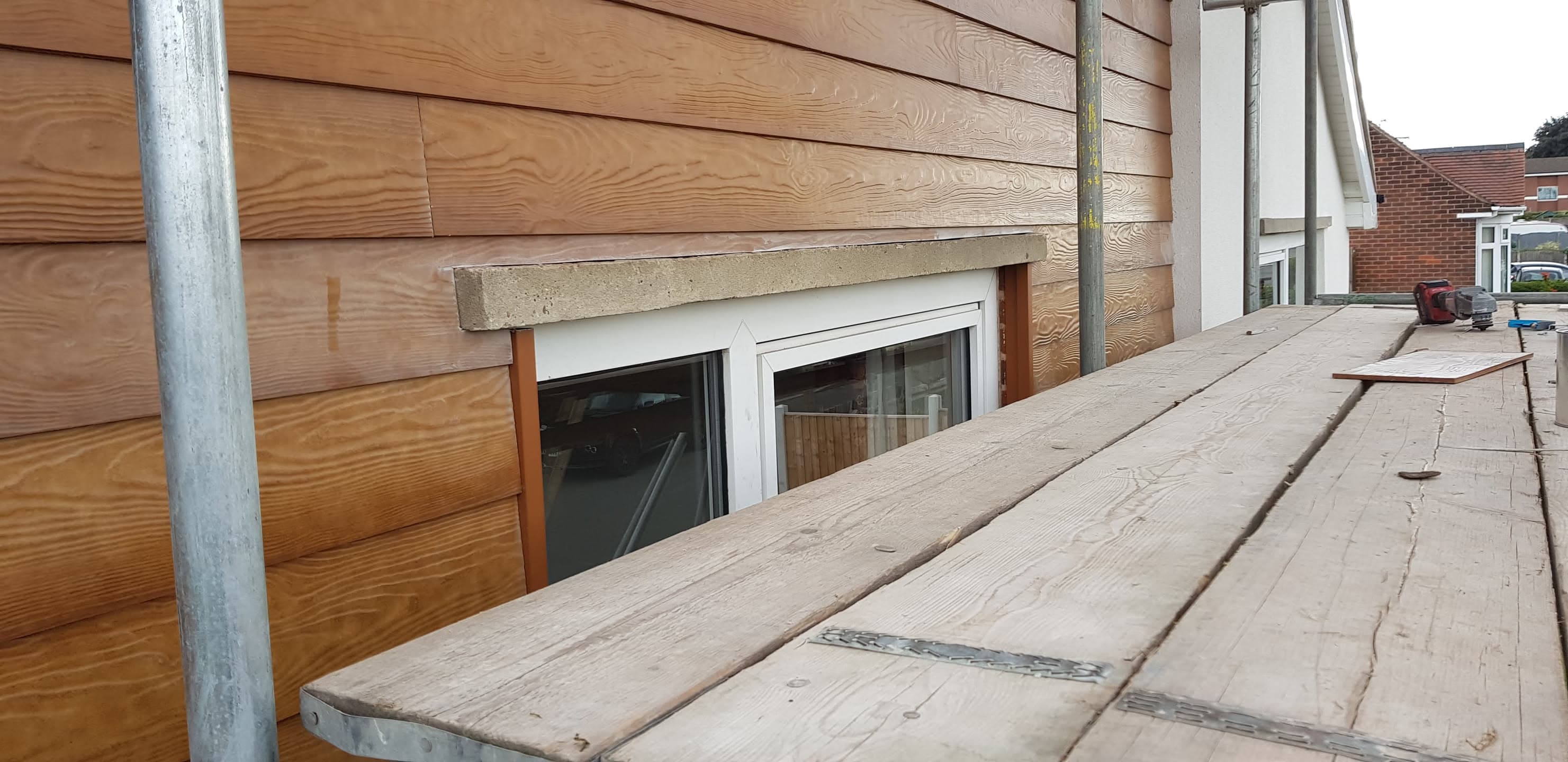Flat roof with timber decking and scaffolding alongside timber-clad building