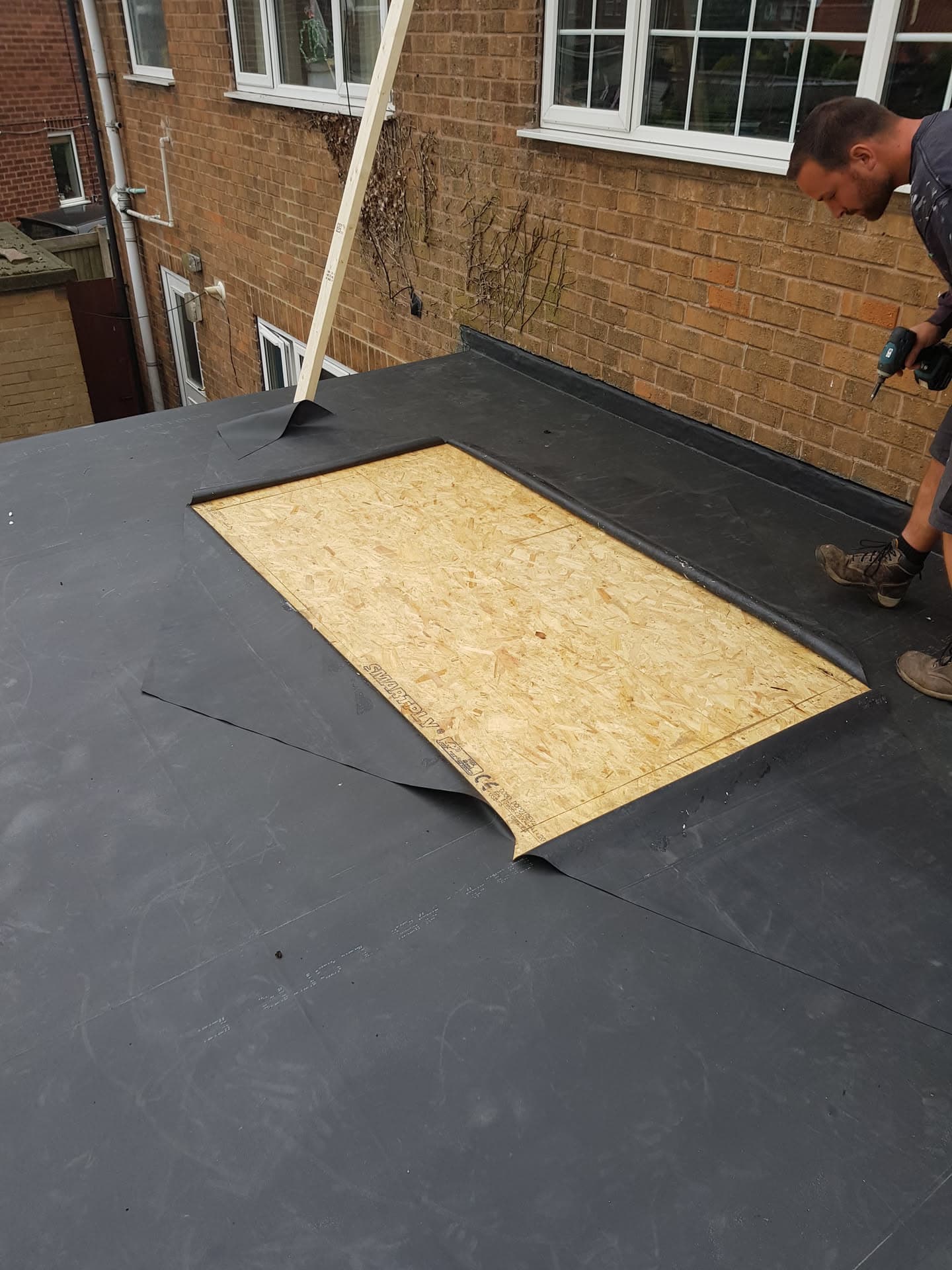 Fitter installing grey felt flat roof with skylight opening on residential extension