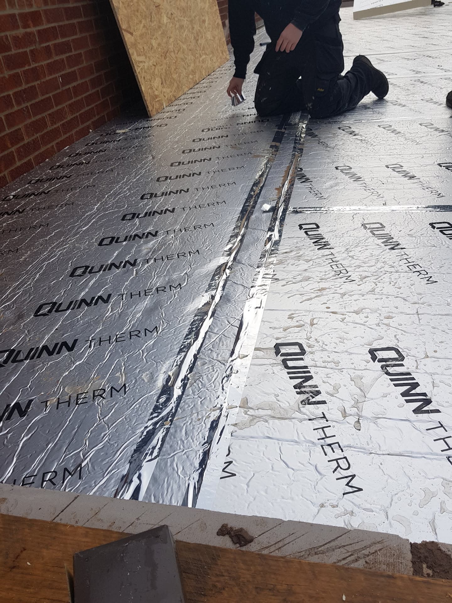 Fitter installing reflective insulation membrane on flat roof deck