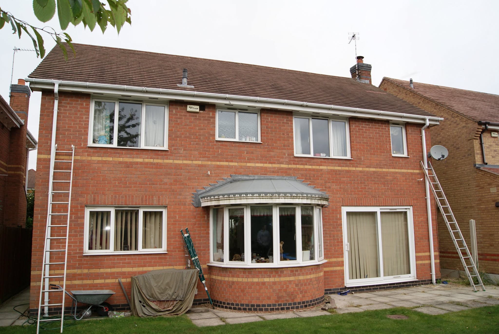 Two-storey brick house with brown concrete tiled pitched roof, white fascias and guttering, chimney stack visible