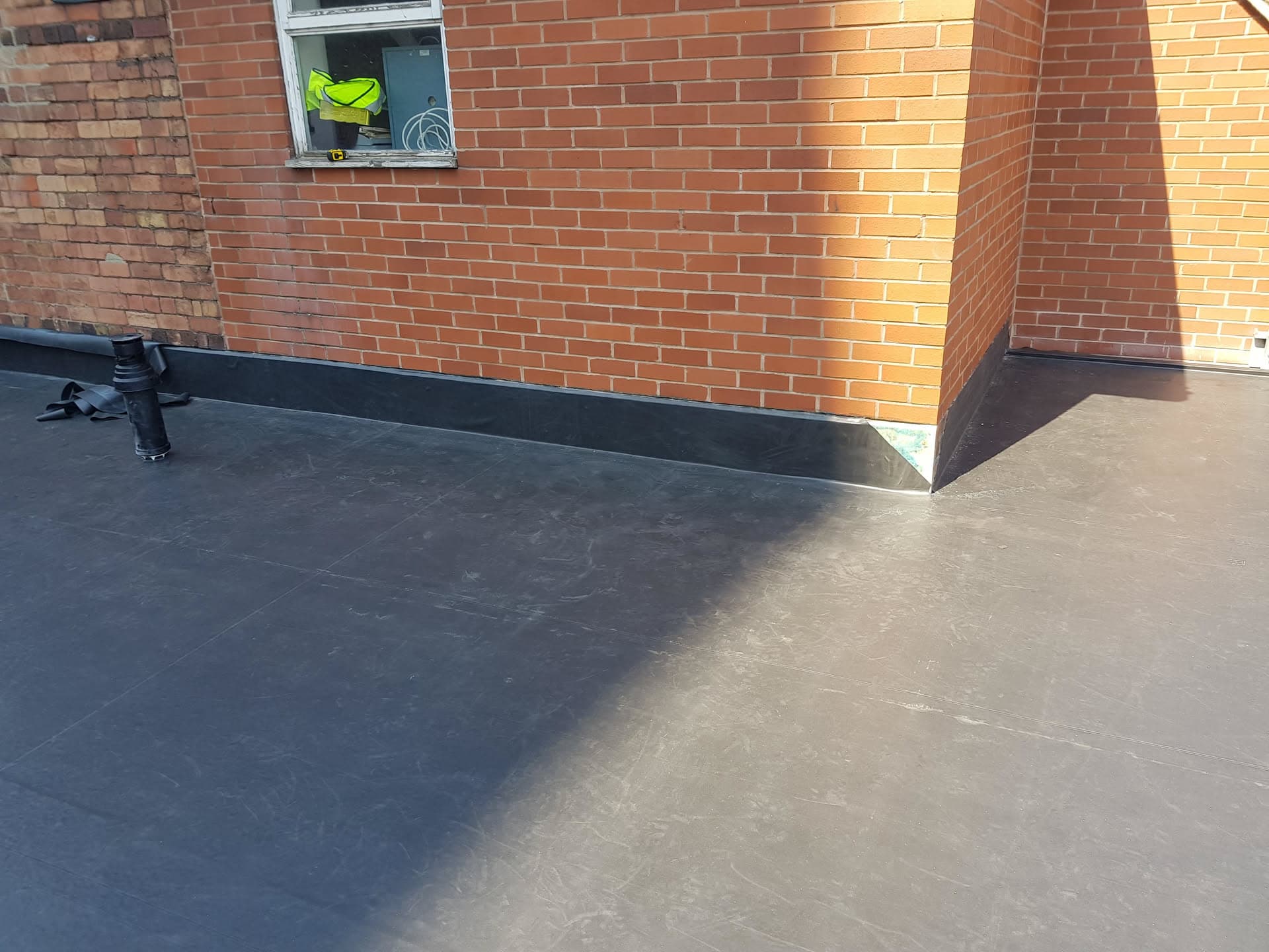 Flat roof with grey felt membrane around brick chimney stack
