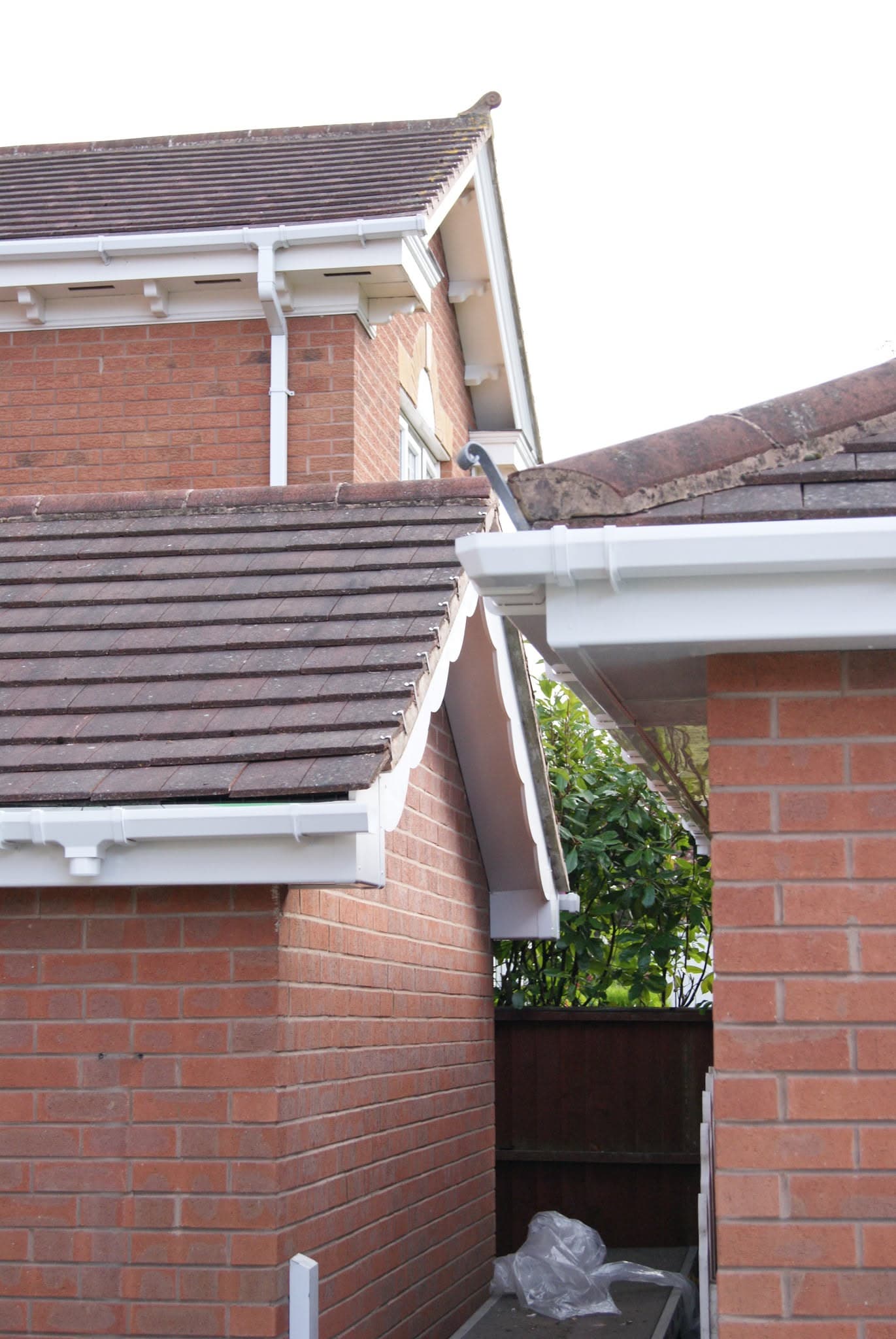 Pitched tiled roof with white fascias, soffits and guttering on red brick house
