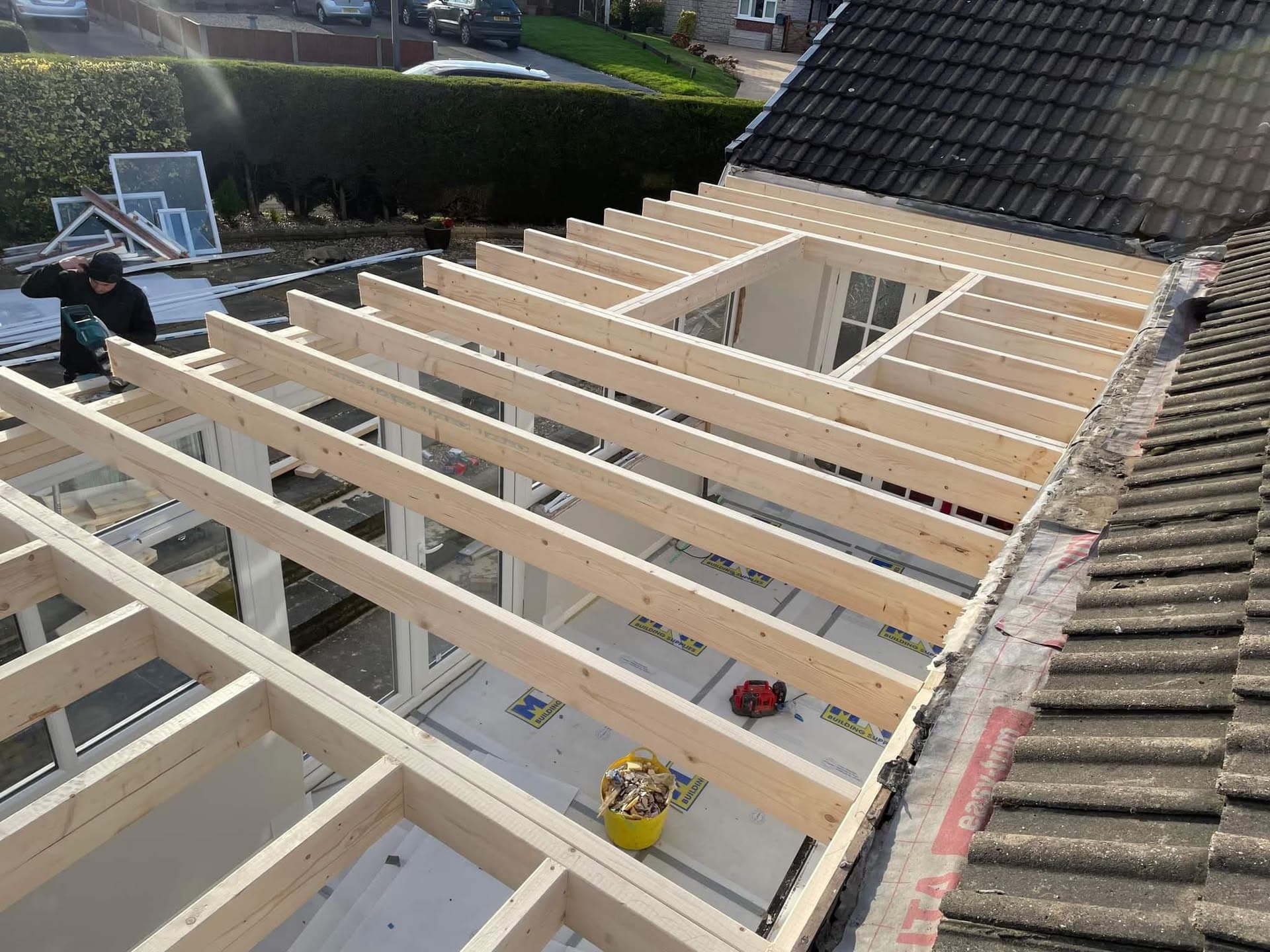 Timber frame construction for flat roof extension adjoining existing tiled pitched roof with fitter working