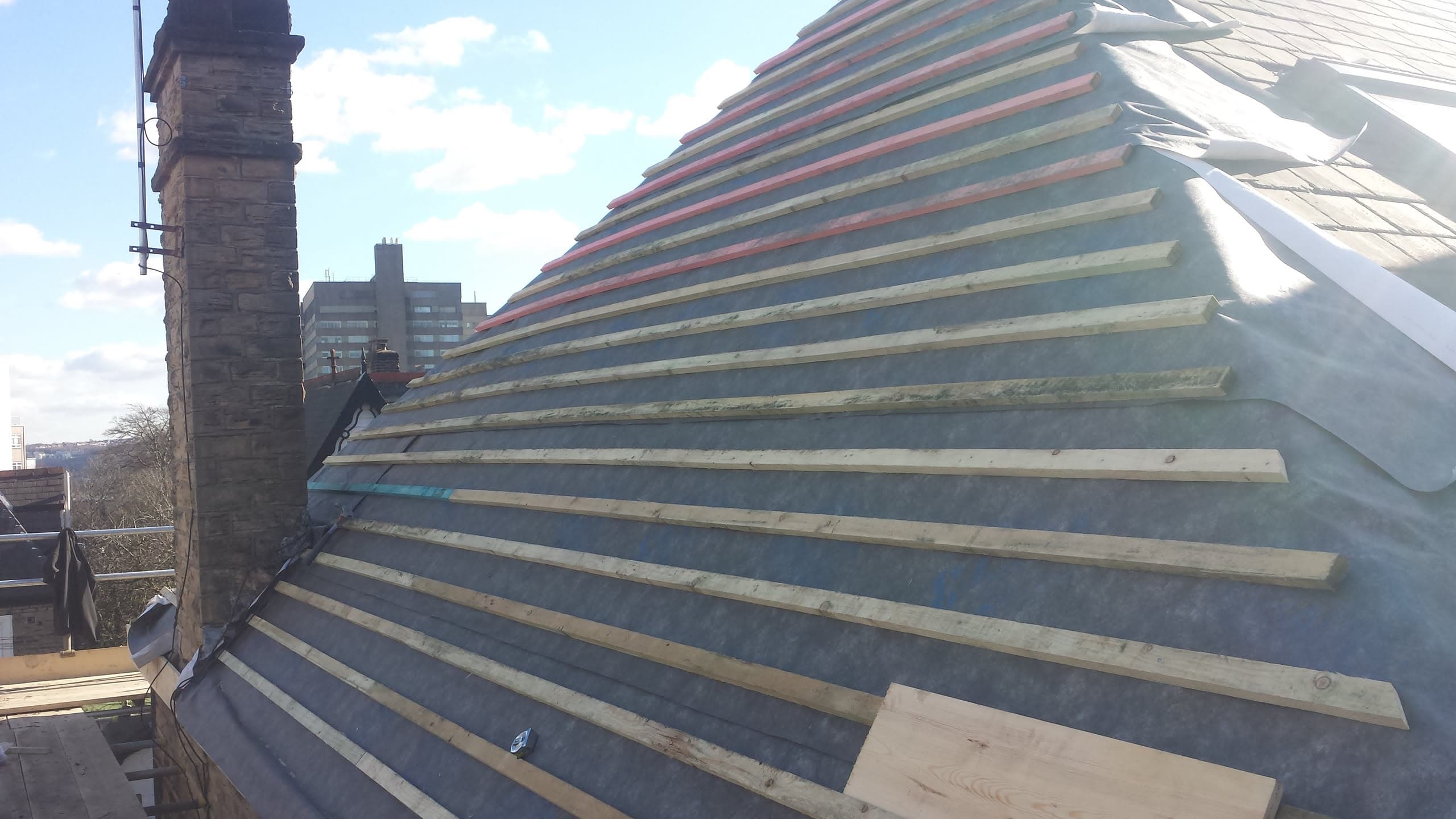 Pitched roof with timber battens and breathable membrane during re-roofing work, chimney stack visible