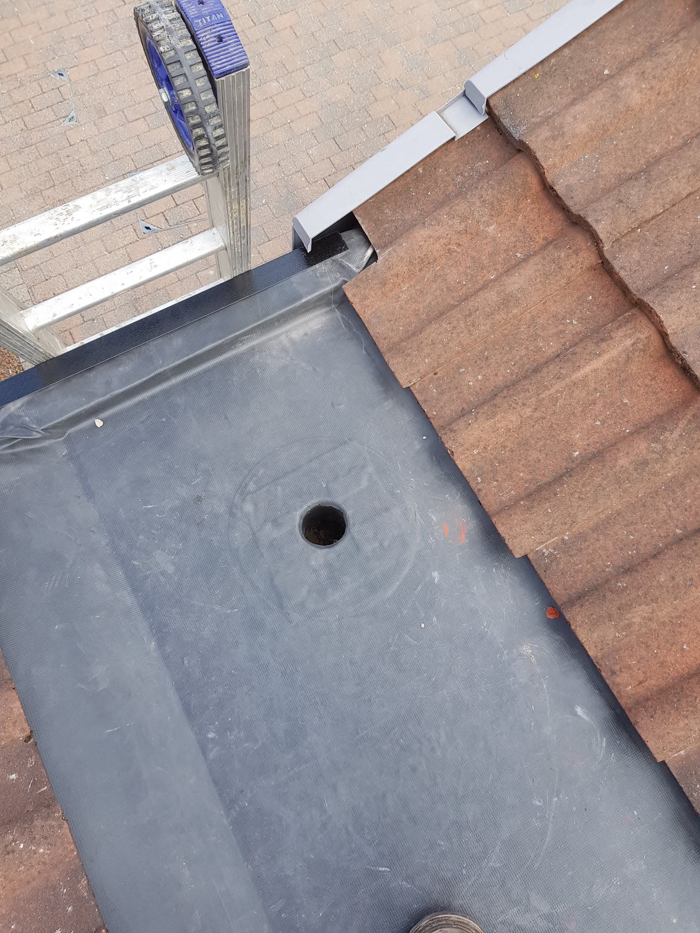 Flat roof with grey EPDM rubber membrane meeting brown concrete tiled pitched roof with white fascia