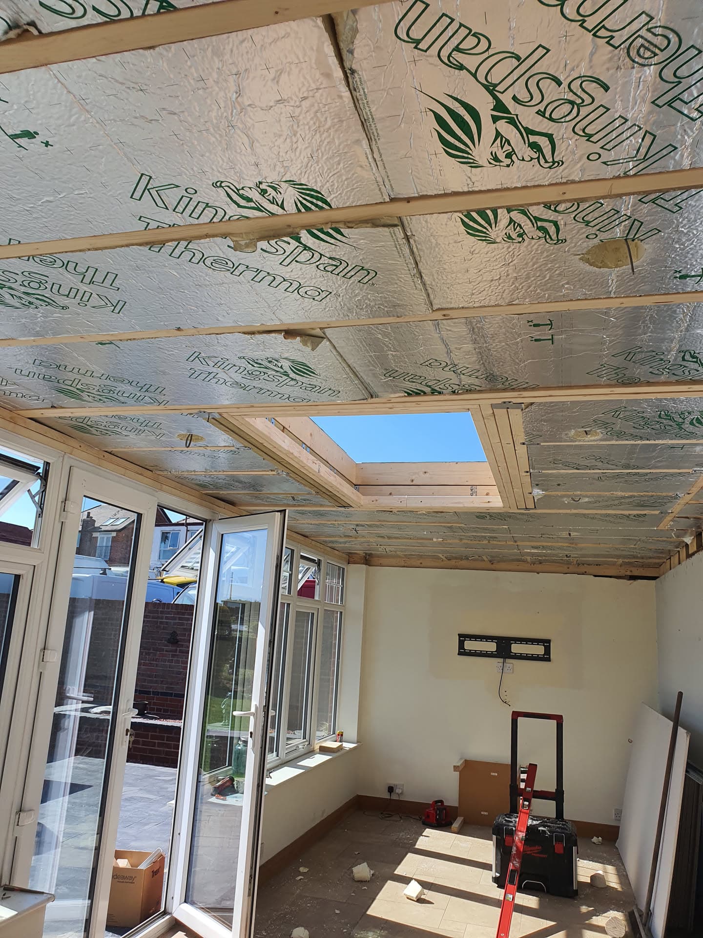 Interior view of conservatory roof installation with exposed timber frame, insulation boards and skylight window