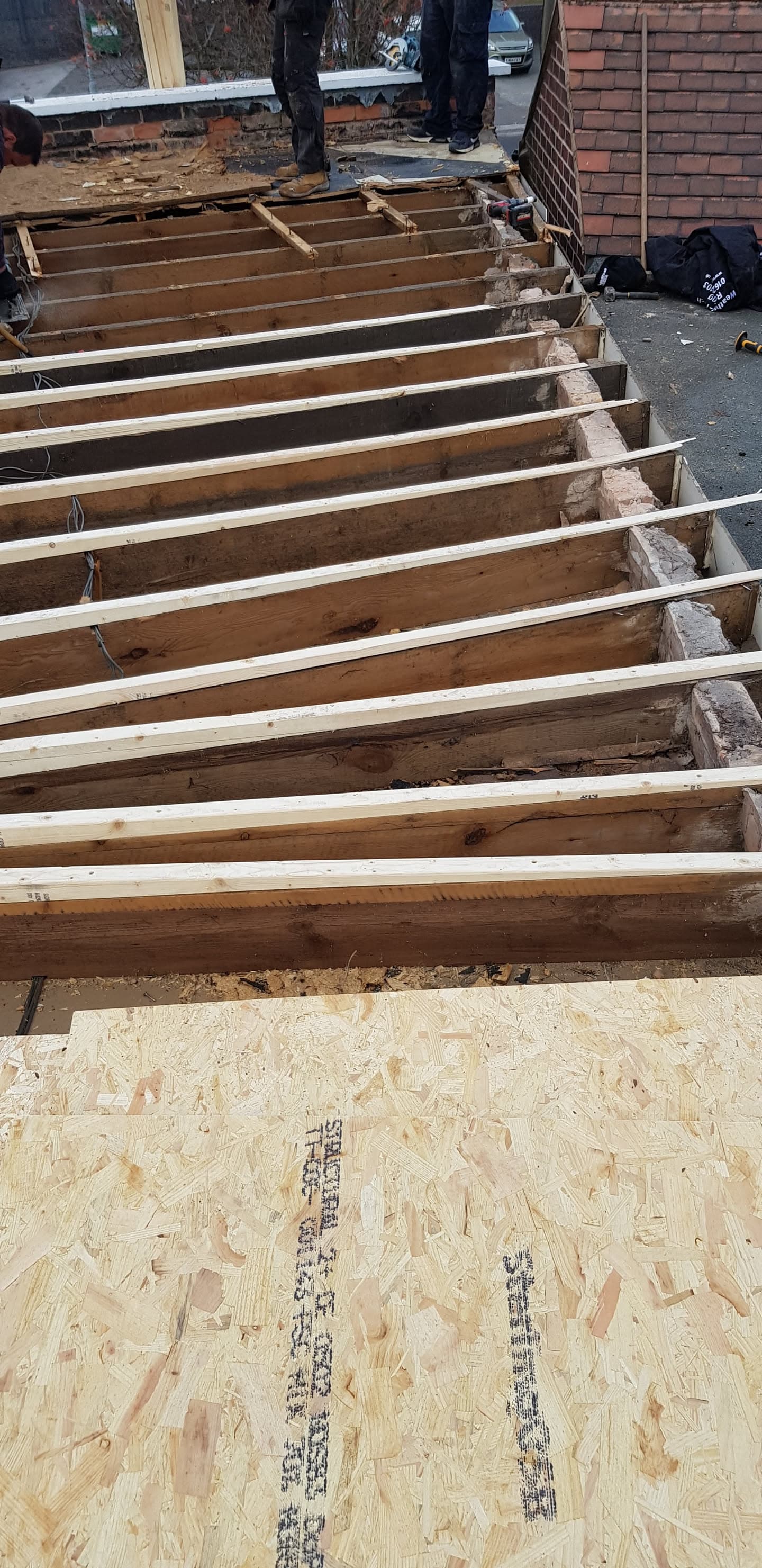 Exposed timber joists on flat roof extension with OSB boarding and fitter working