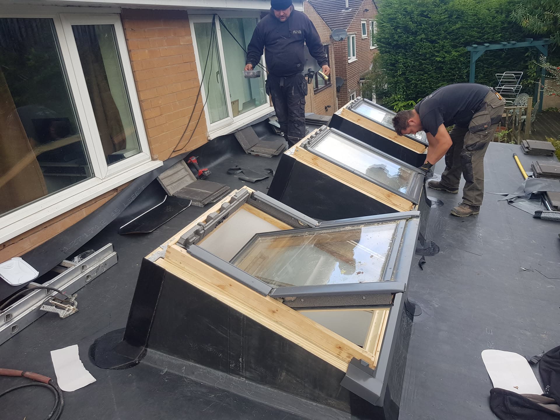 Two fitters installing roof windows on a flat roof with black felt membrane