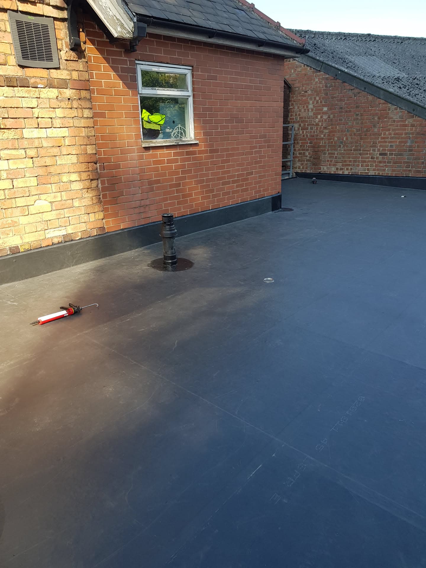 Completed flat roof installation with grey rubber membrane and drainage outlets on brick building