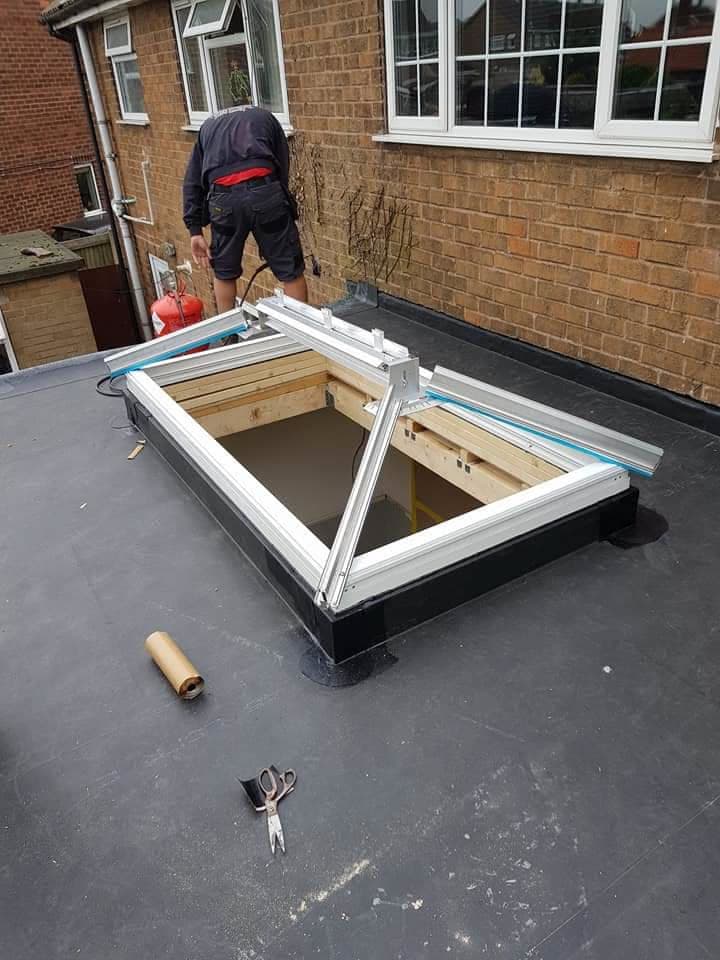 Fitter installing white uPVC roof lantern on flat roof with black felt covering
