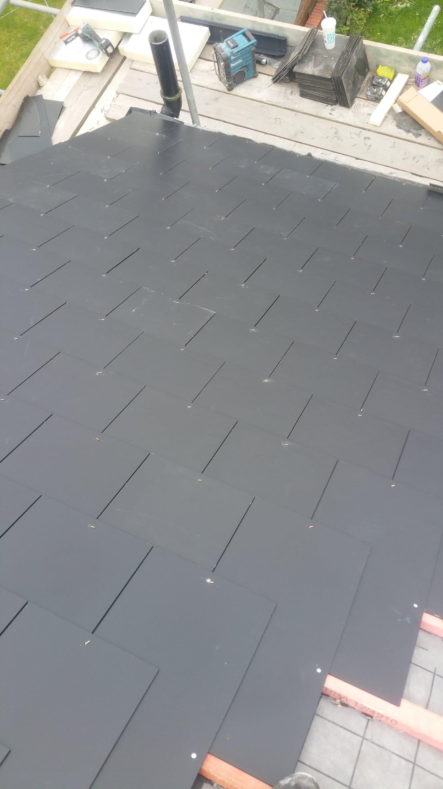 Newly installed dark grey slate pitched roof with black soil pipe and timber framework visible