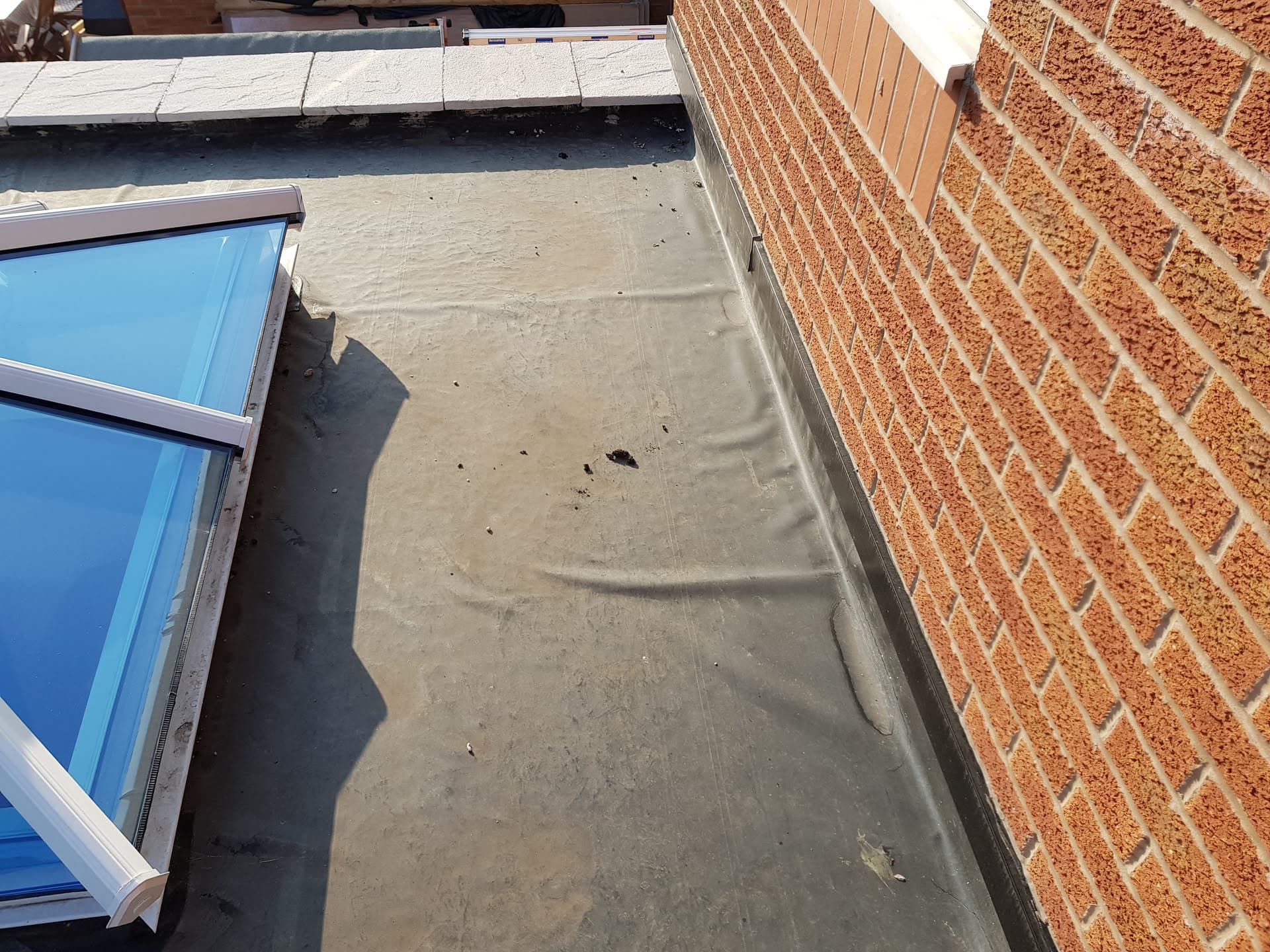 Flat roof with grey EPDM rubber membrane alongside brick wall and skylight