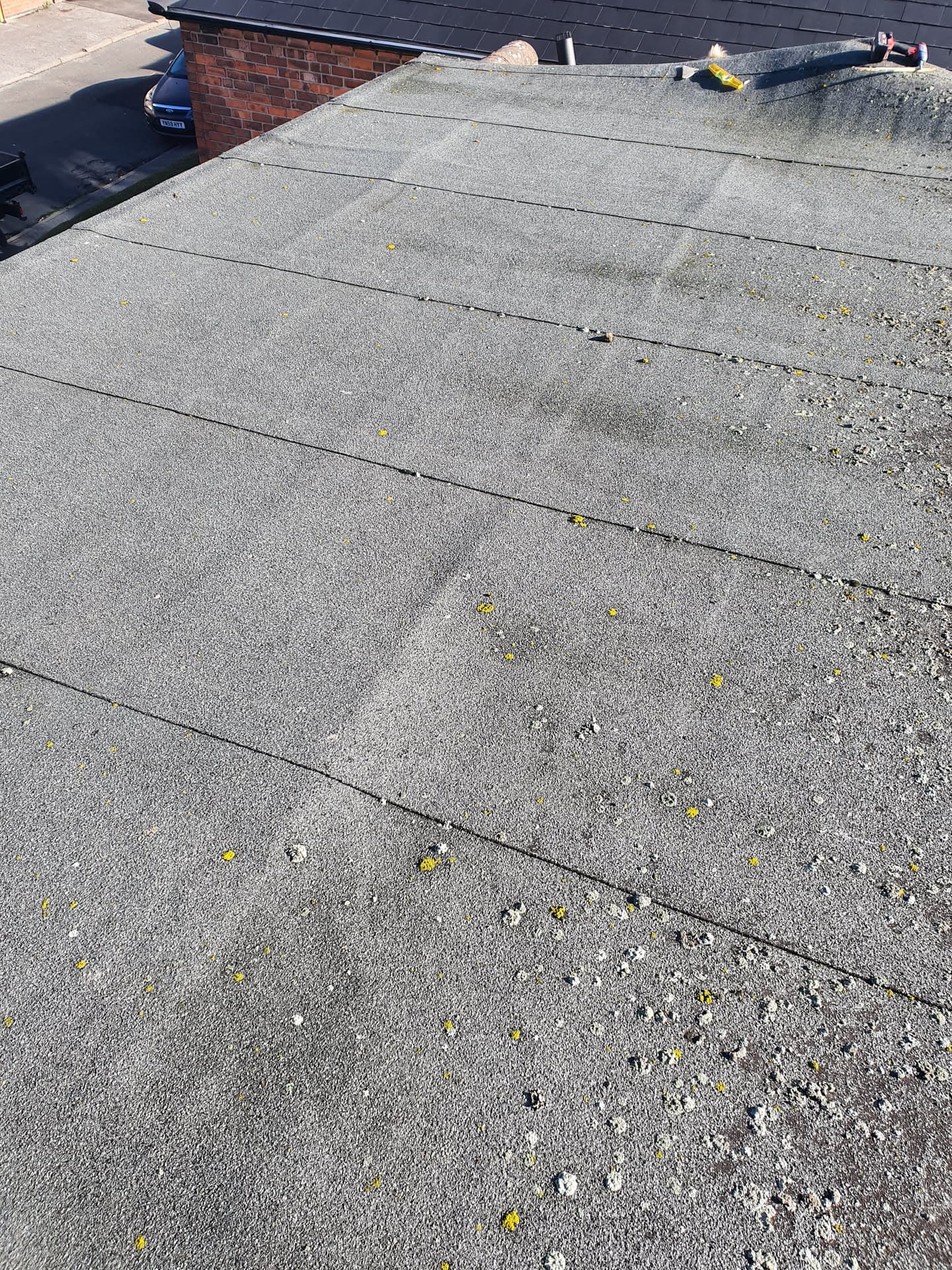 Flat roof with grey felt covering showing weathering and moss growth, brick chimney visible