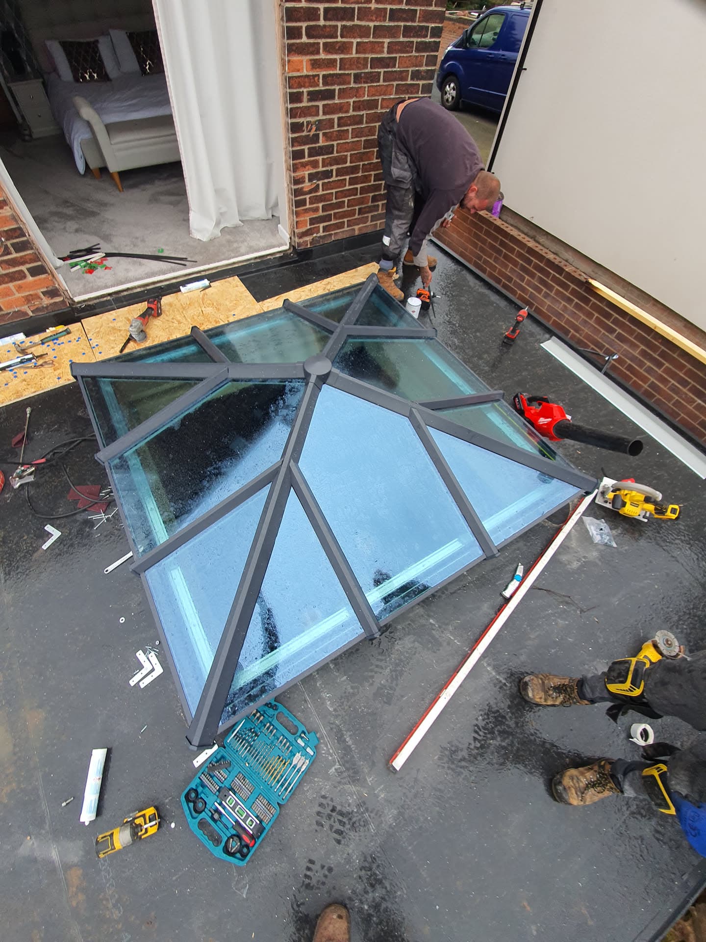 Fitter installing glass roof lantern on flat roof with anthracite frame and surrounding tools