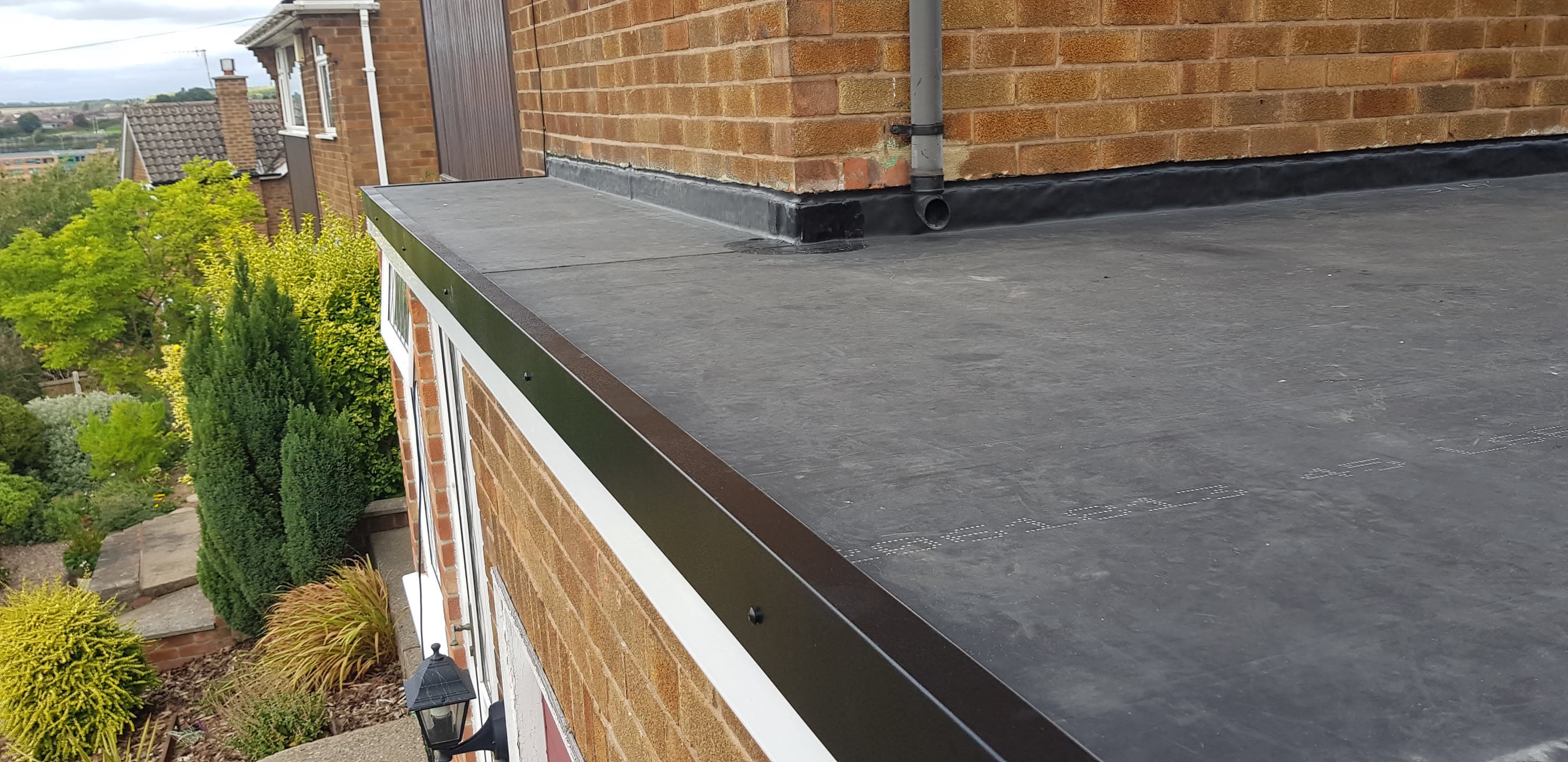 Flat roof with dark grey felt membrane and metal fascia trim on residential extension