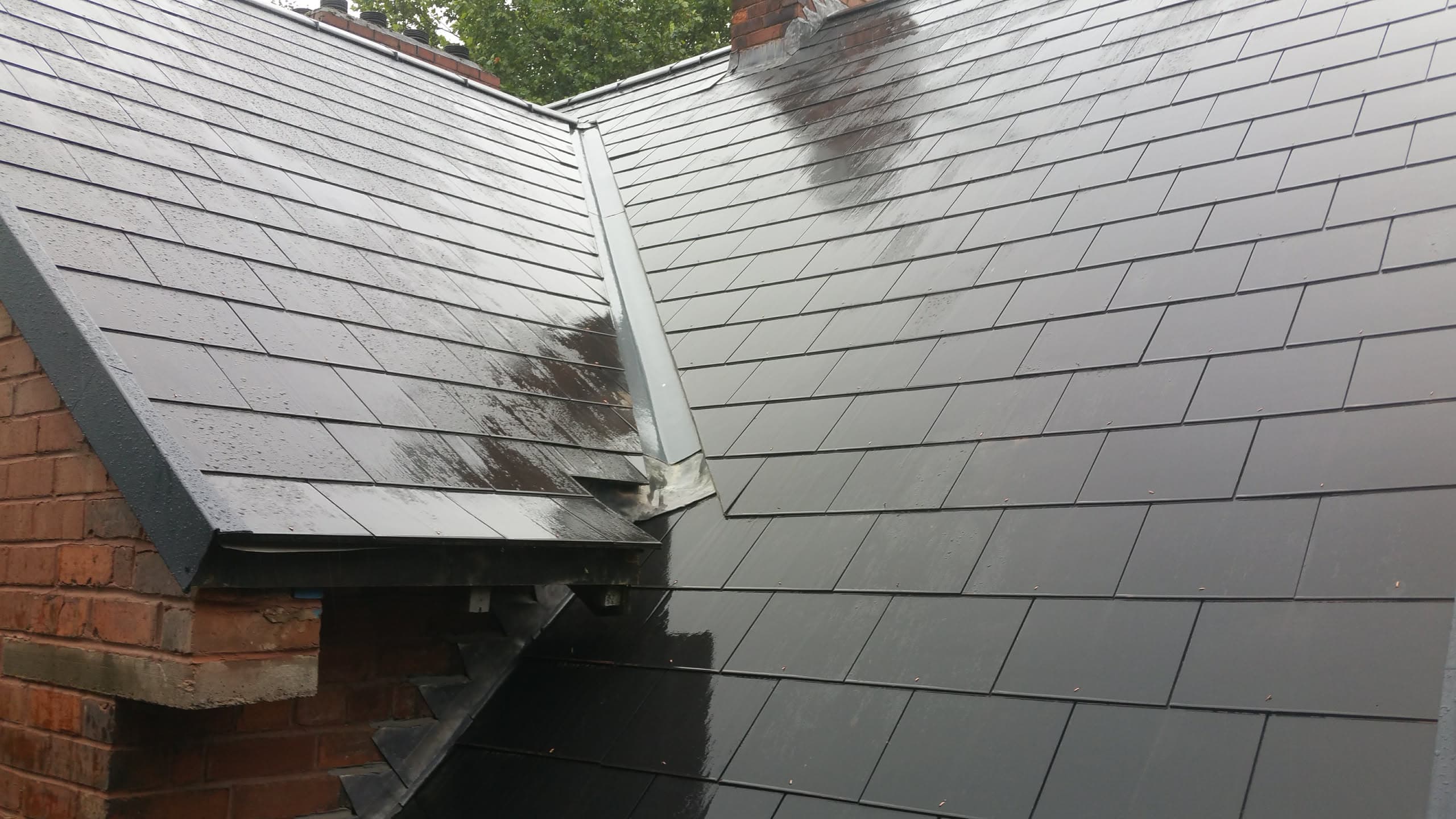 Grey slate pitched roof with white fascias and lead valley flashing between two roof sections