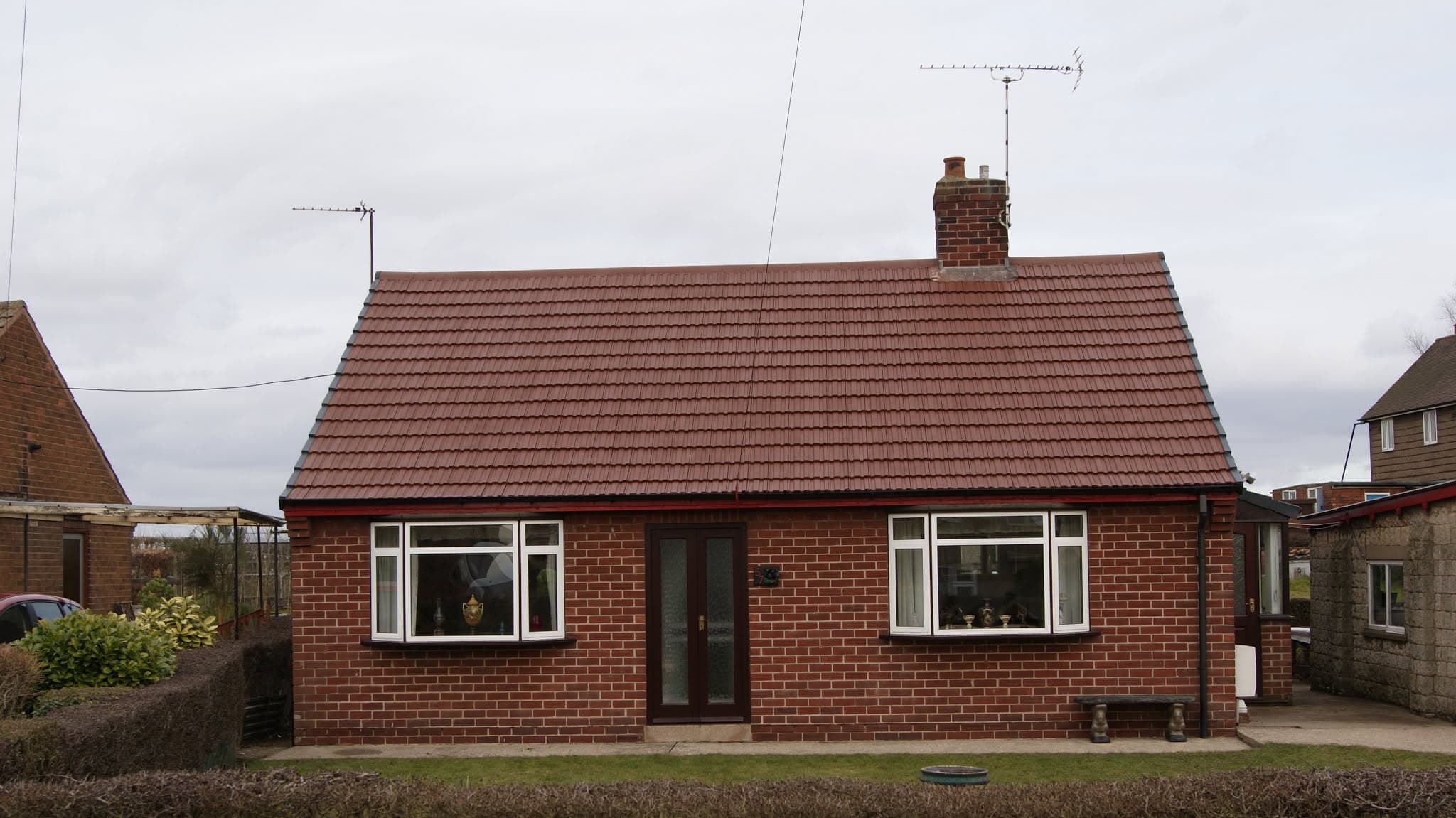 Pitched roof with red concrete tiles and brick chimney stack on red brick bungalow