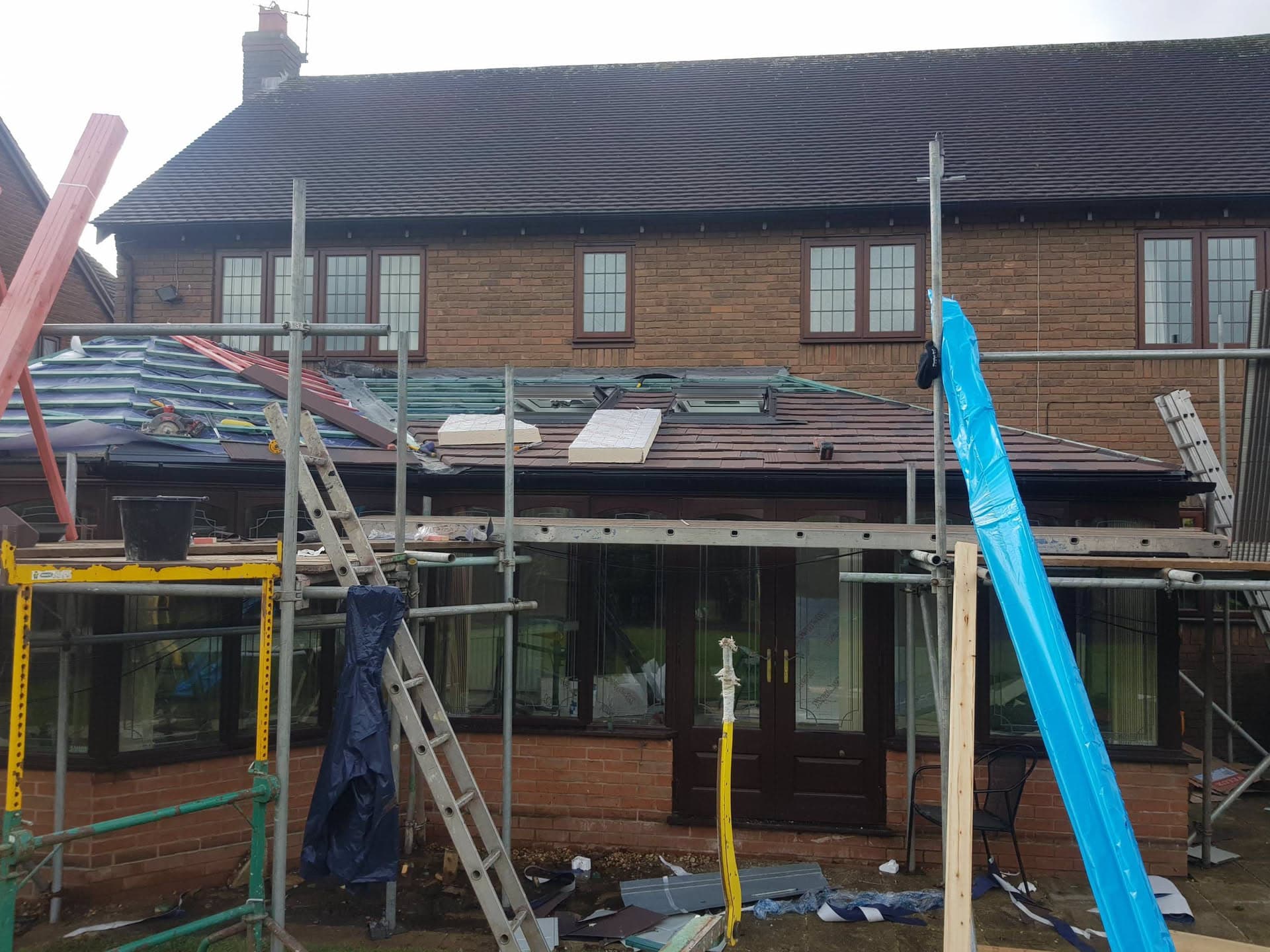 Flat roof extension under construction with metal framework and partial brown tiled covering, scaffolding erected