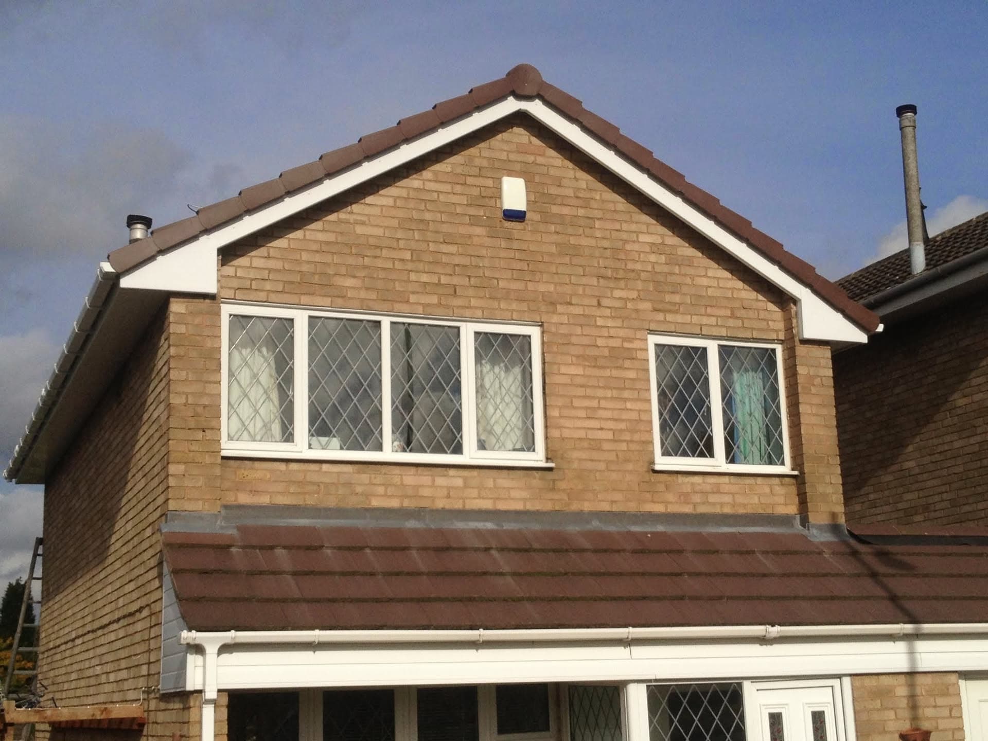 Pitched roof with brown concrete tiles, white fascias and guttering on brick house