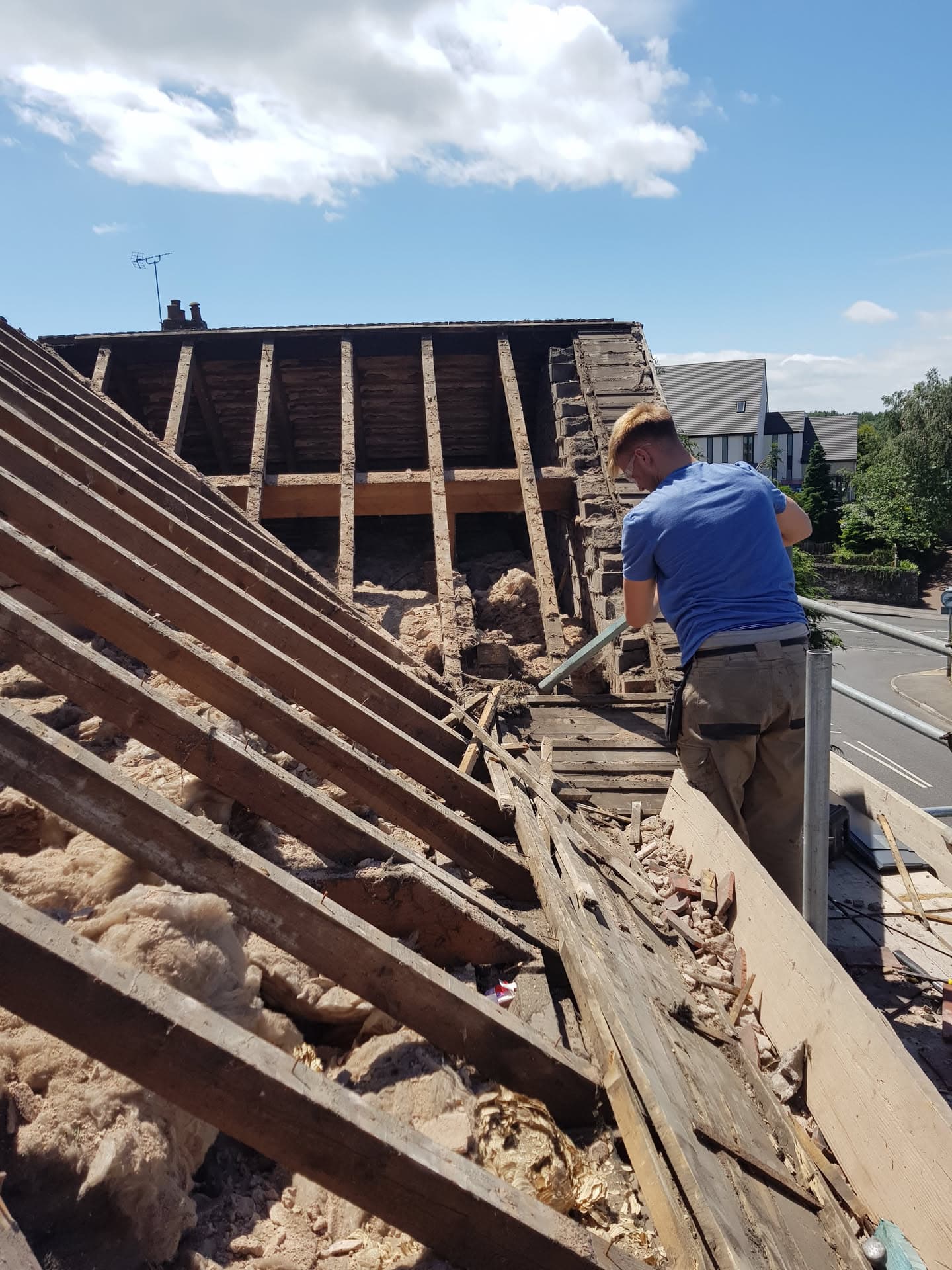 Fitter working on pitched roof with exposed timber battens and chimney stack during re-roofing