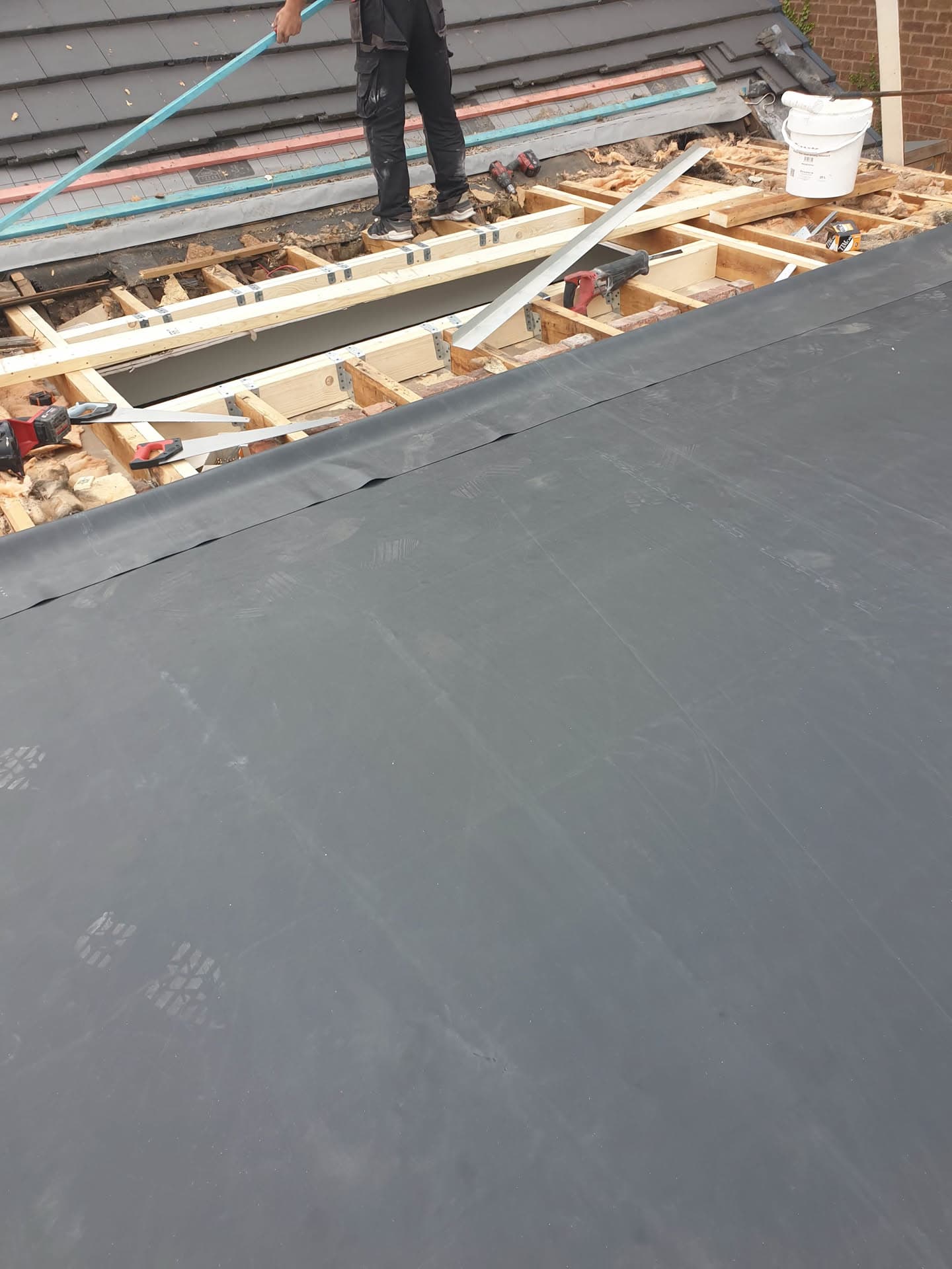 Pitched roof installation in progress with grey felt membrane and exposed timber battens, fitter working