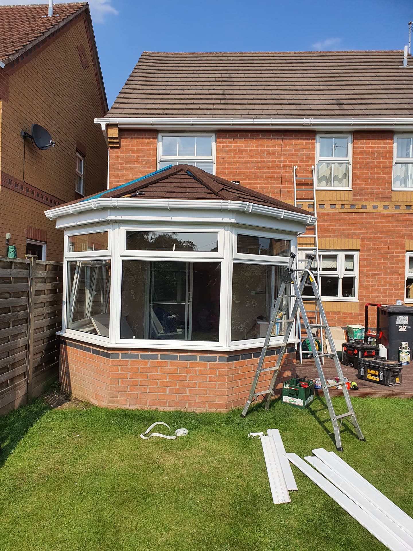 Brown tiled conservatory roof with white fascias and guttering on brick house