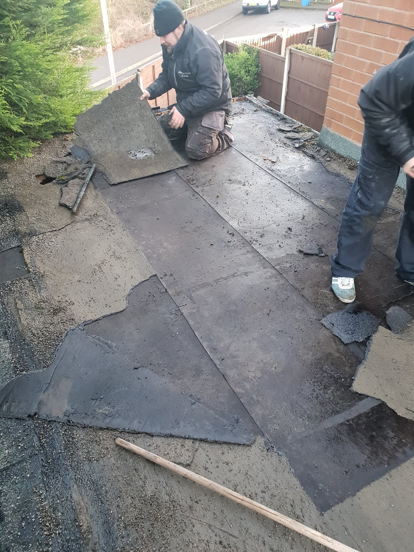 Fitters installing dark grey felt sheets on a flat roof