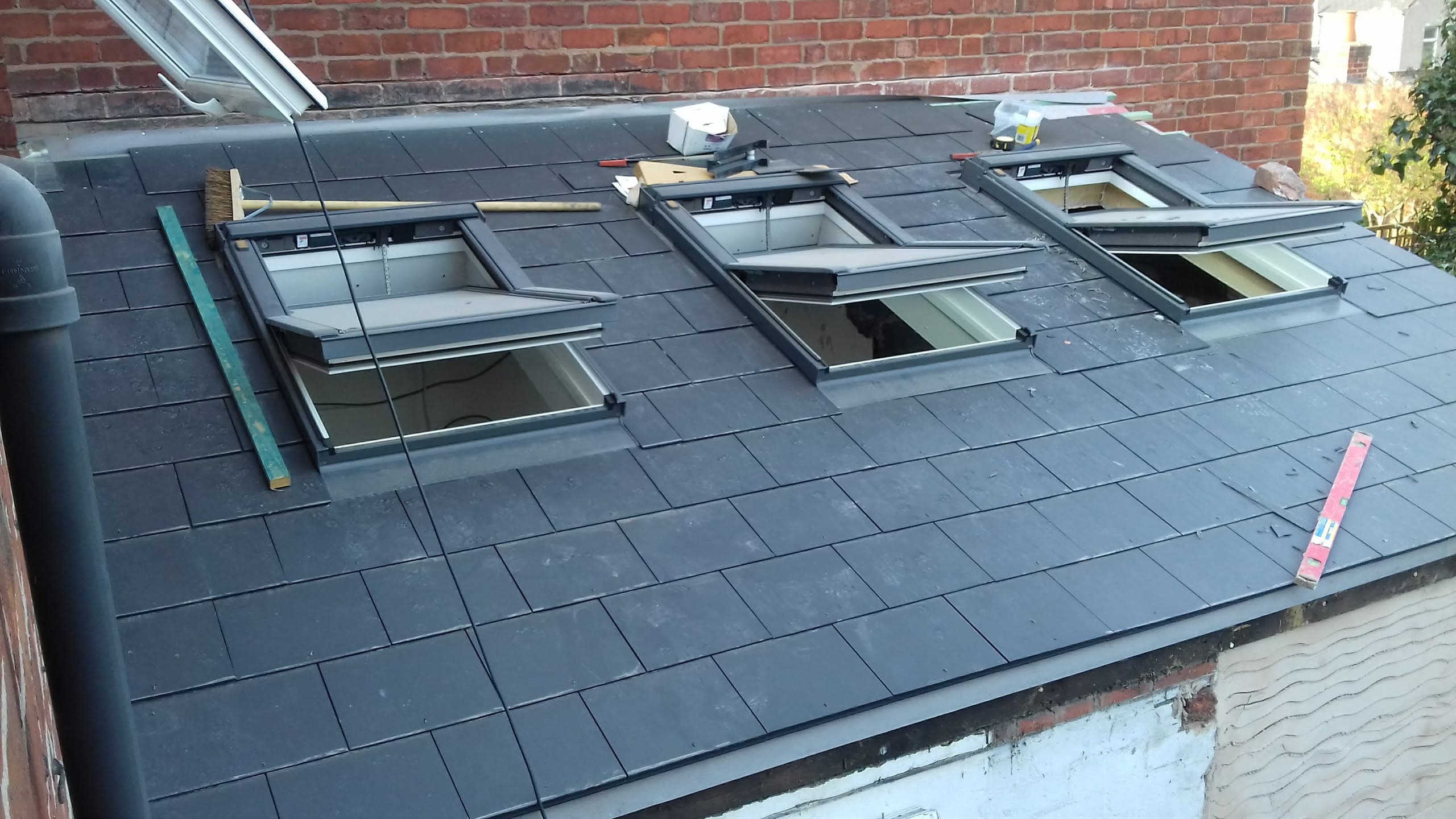 Pitched roof with dark grey slate tiles and four roof windows being installed