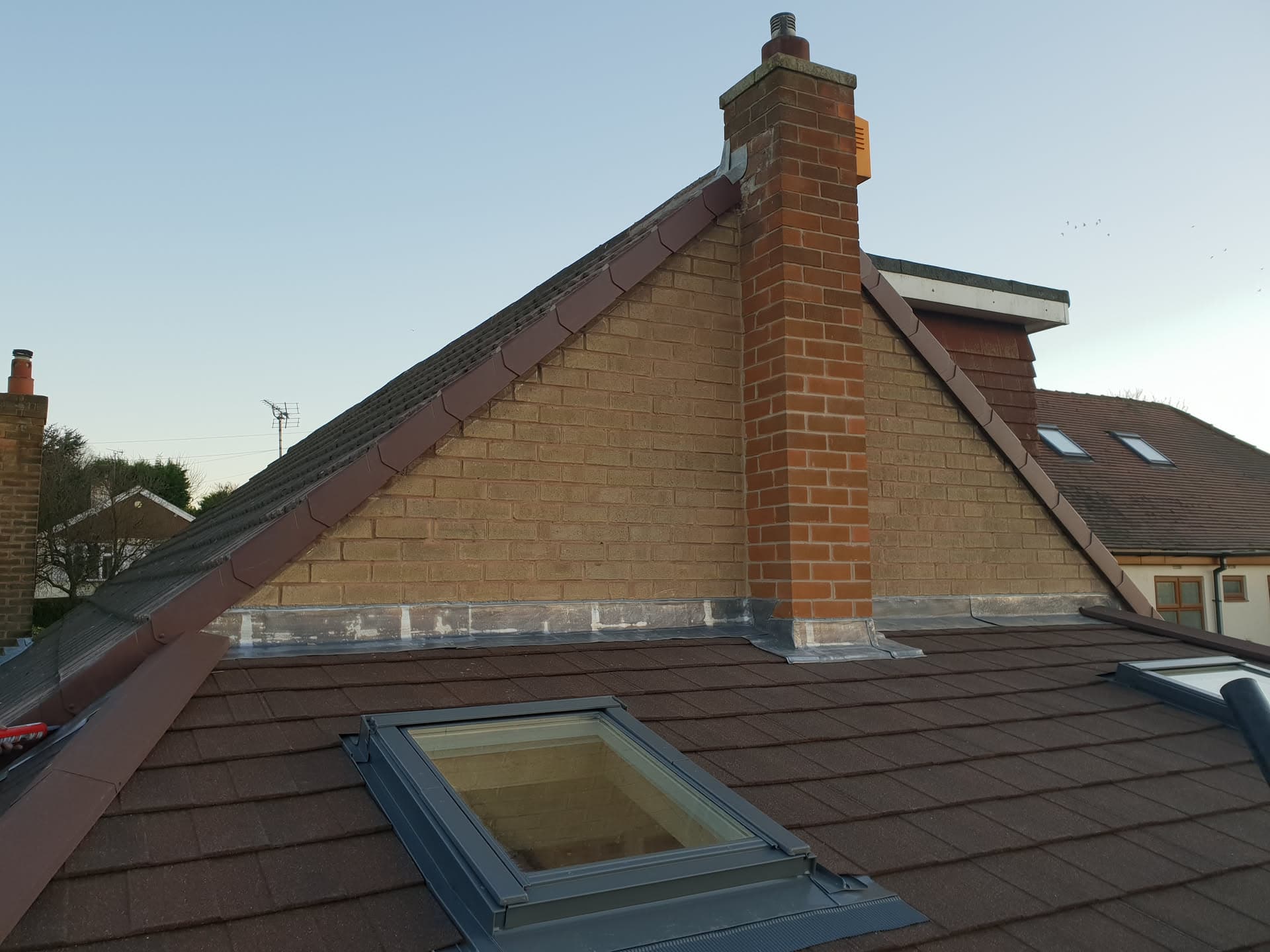 Pitched roof with brown concrete tiles, lead flashing and brick chimney stack
