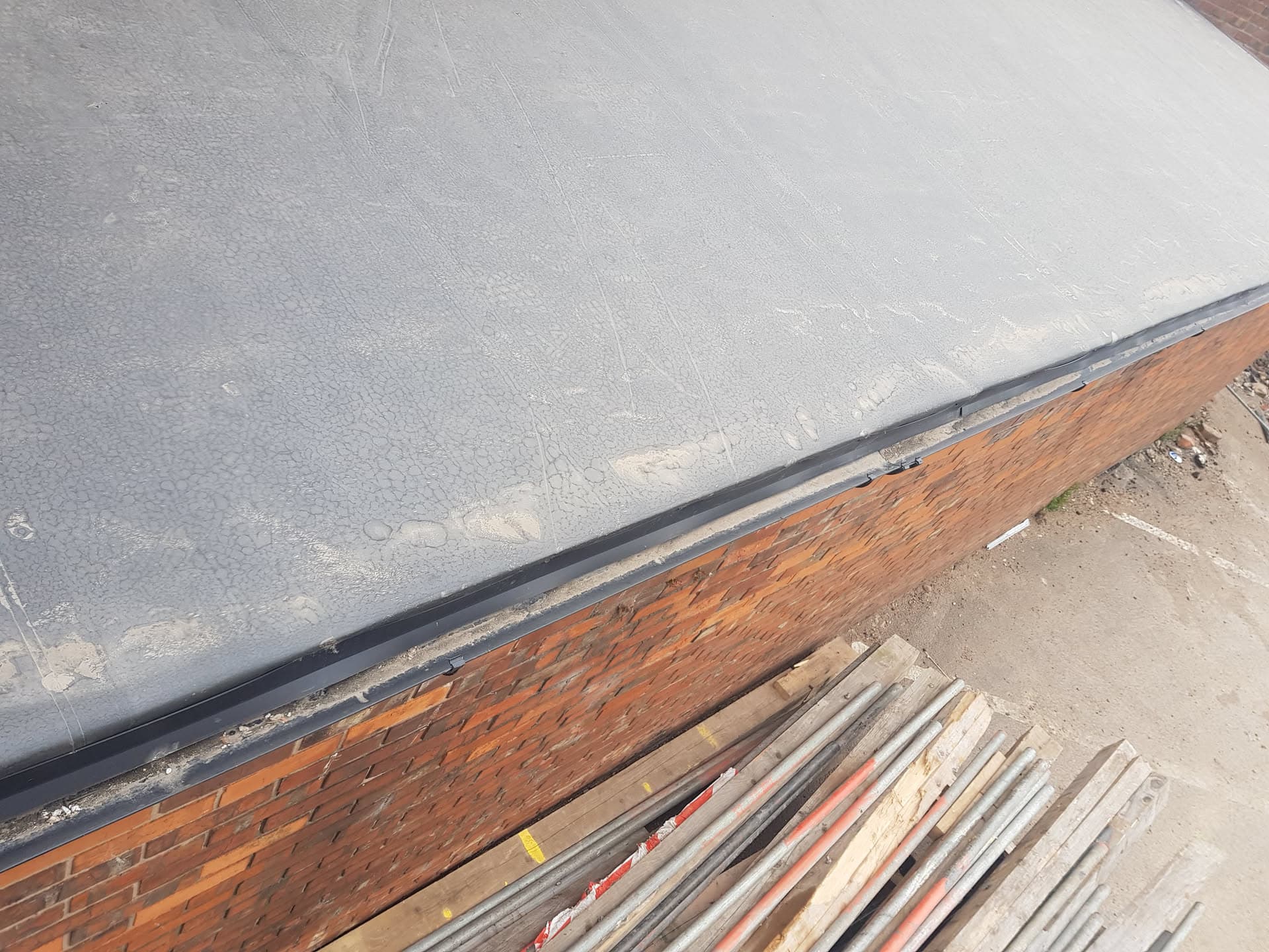 Grey GRP flat roof with black fascia board and brick wall detail