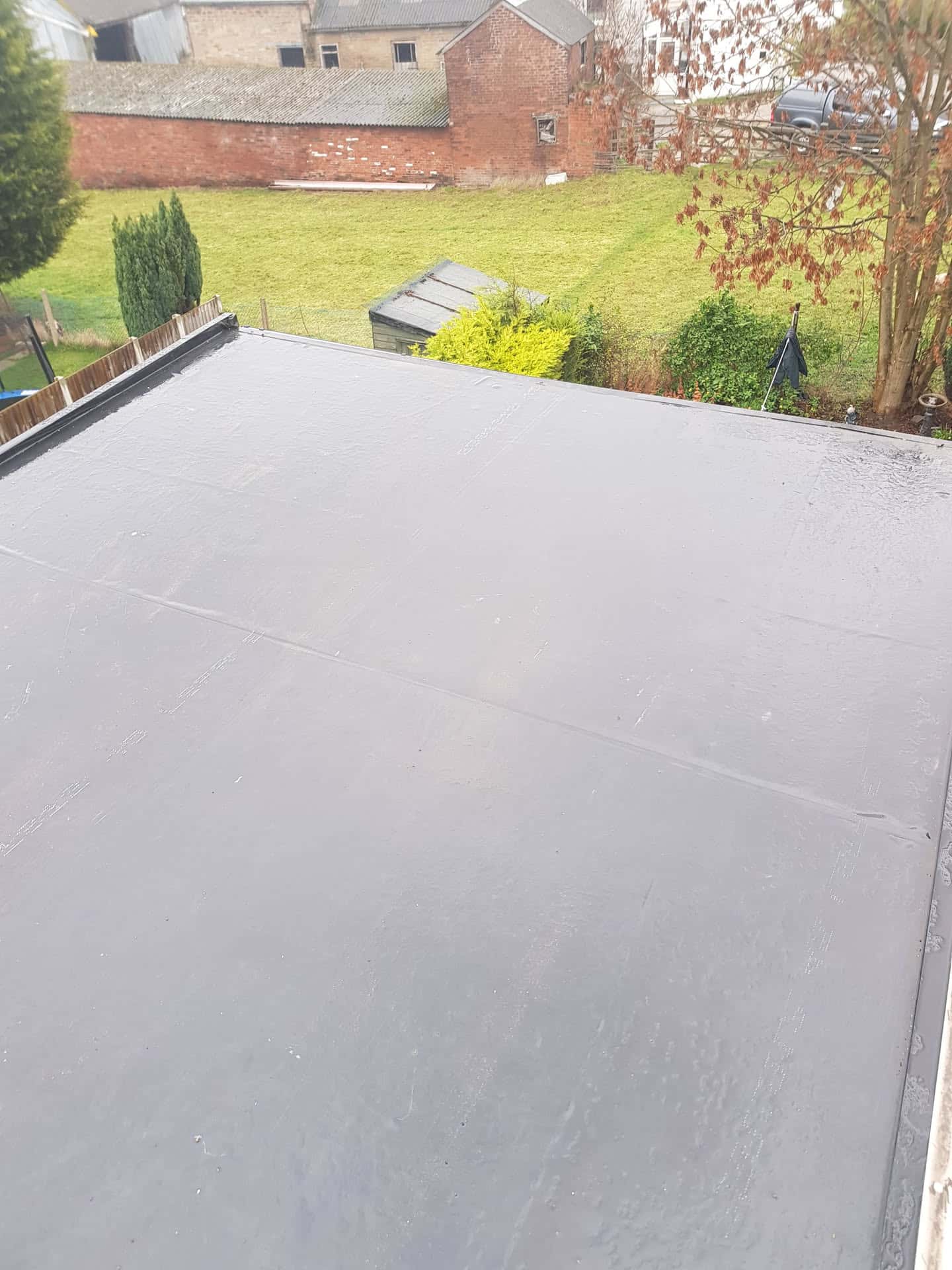 Completed grey EPDM rubber flat roof extension overlooking residential garden